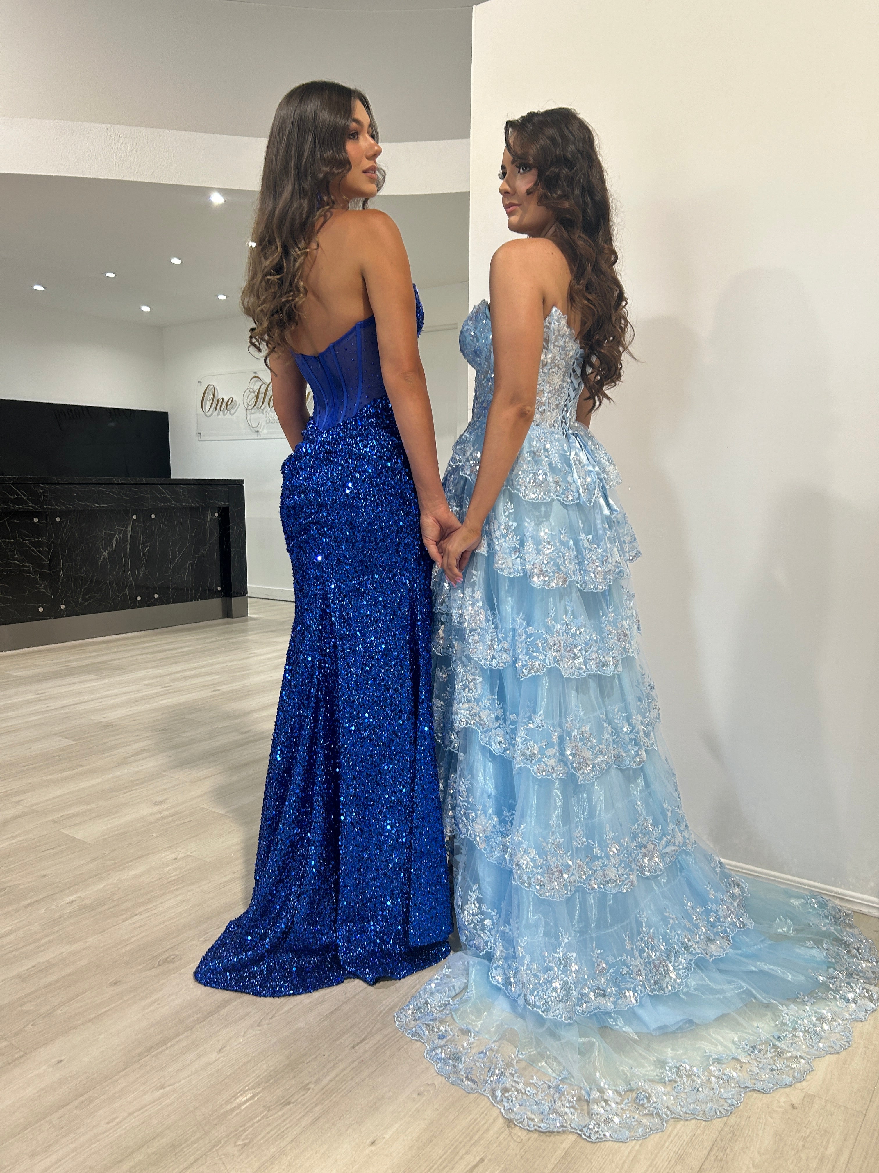 Two women in elegant blue evening gowns from Honey Couture, featuring a strapless sequin design and tiered lace details, by Australian designer.