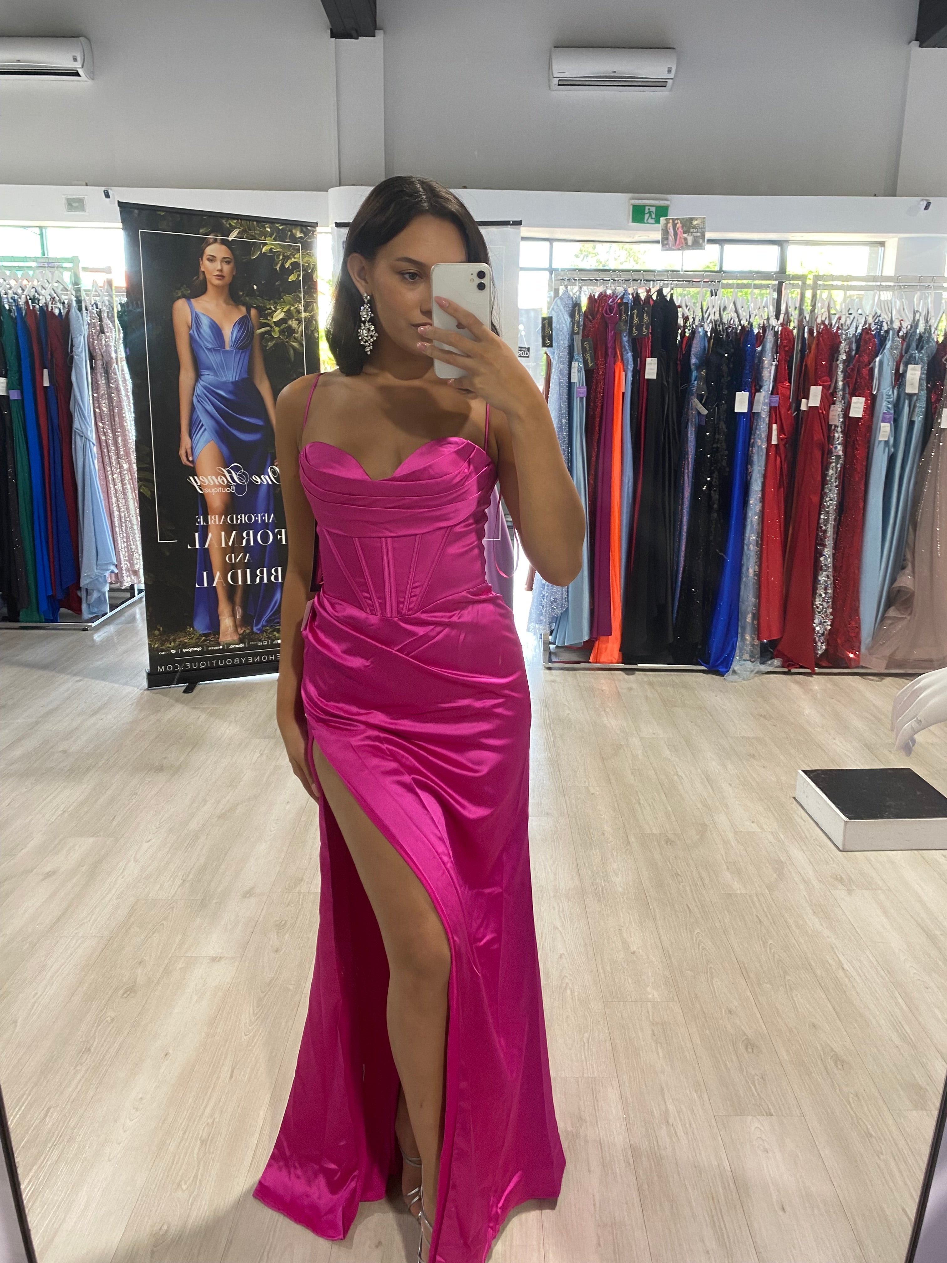 Woman wearing pink satin corset school formal dress with leg split, taking a mirror selfie in a boutique. Brisbane to Gold Coast.