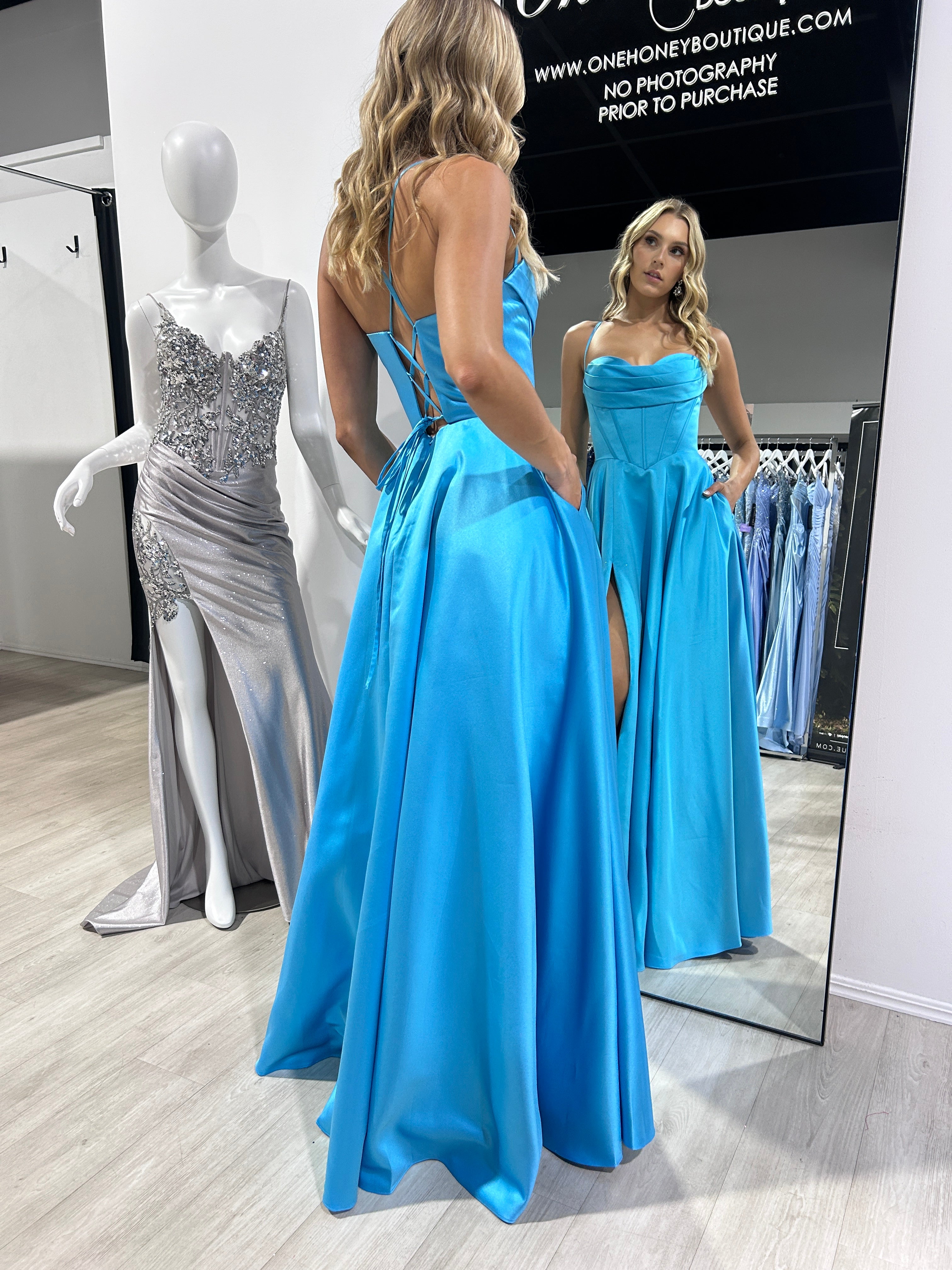 Woman wearing Honey Couture BRIELLA Satin Corset Ball Gown in blue, showcasing elegant designer prom dress with mirror reflection.