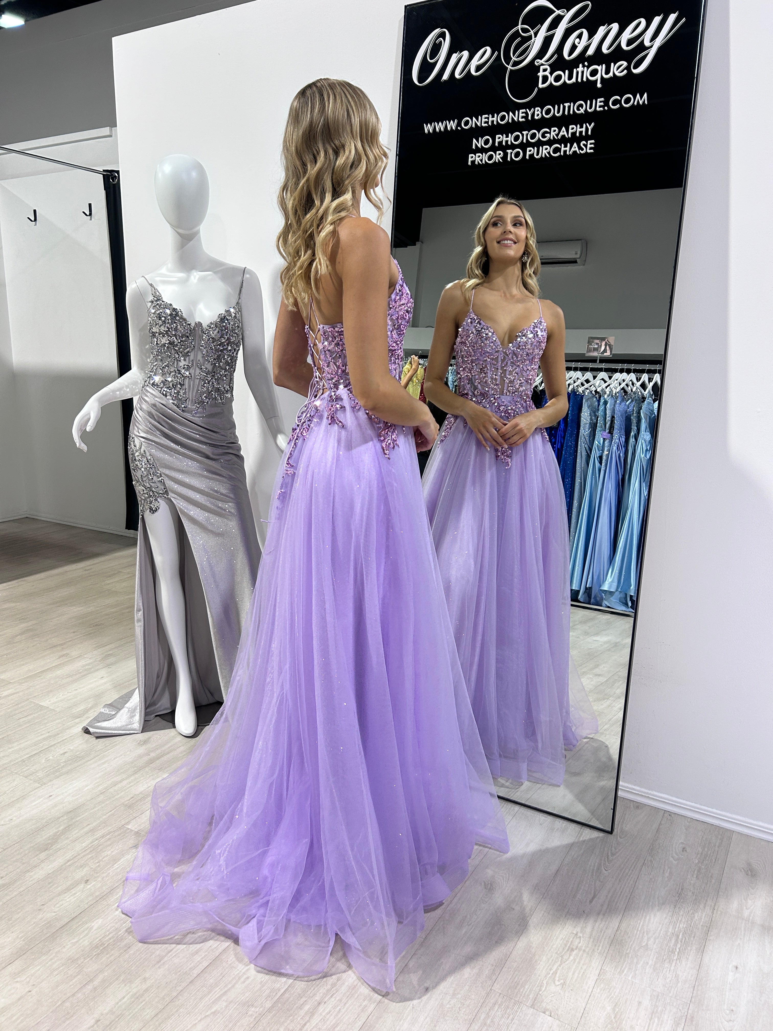 Woman in lavender tulle prom dress admiring reflection in One Honey Boutique mirror.