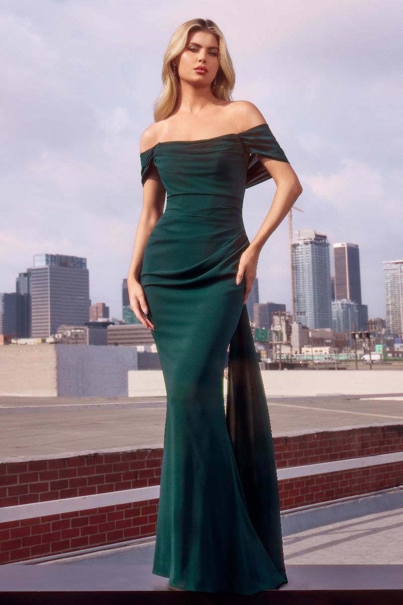 Elegant off-shoulder emerald evening gown with draped sleeves, modeled on a rooftop backdrop, city skyline visible. Perfect for formal events.