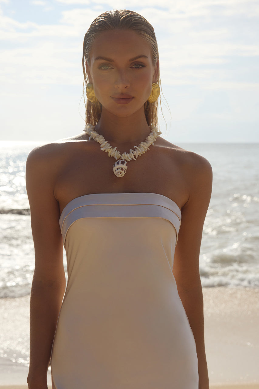 A model wearing a strapless dress with a folded neckline and floral necklace, standing on a beach. Perfect for formal occasions in Australia.