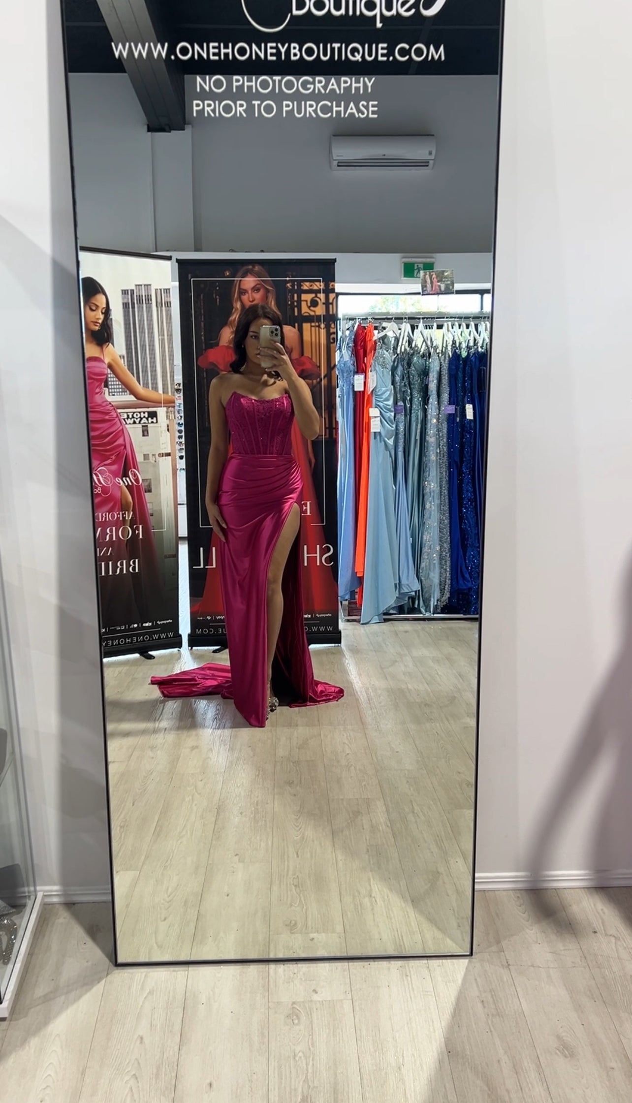 Woman trying on a strapless pink formal dress with a thigh-high slit at a boutique.