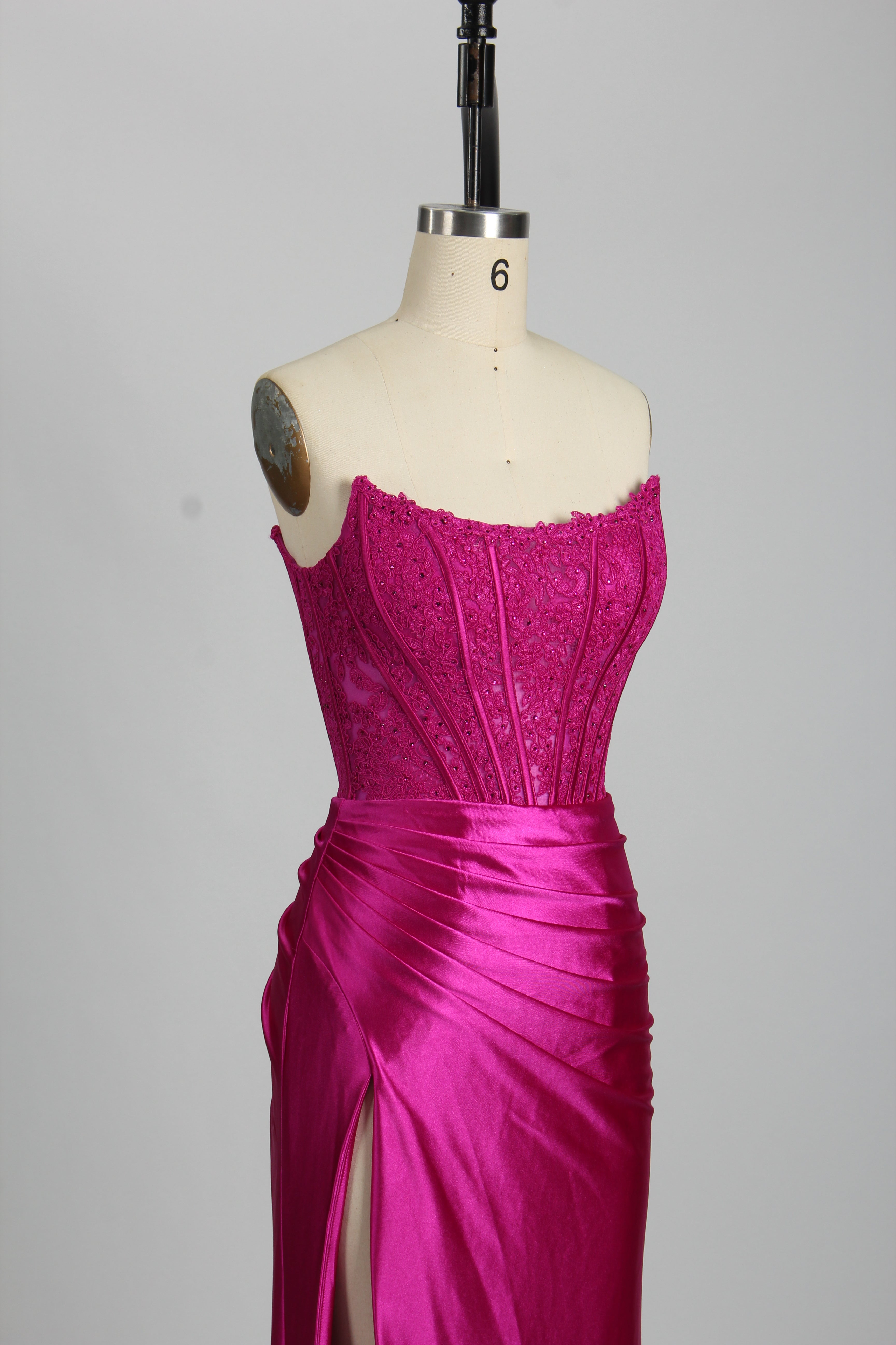 Strapless fuchsia embellished bustier evening gown on mannequin, featuring mermaid cut and satin finish. Perfect for prom or formal occasions.