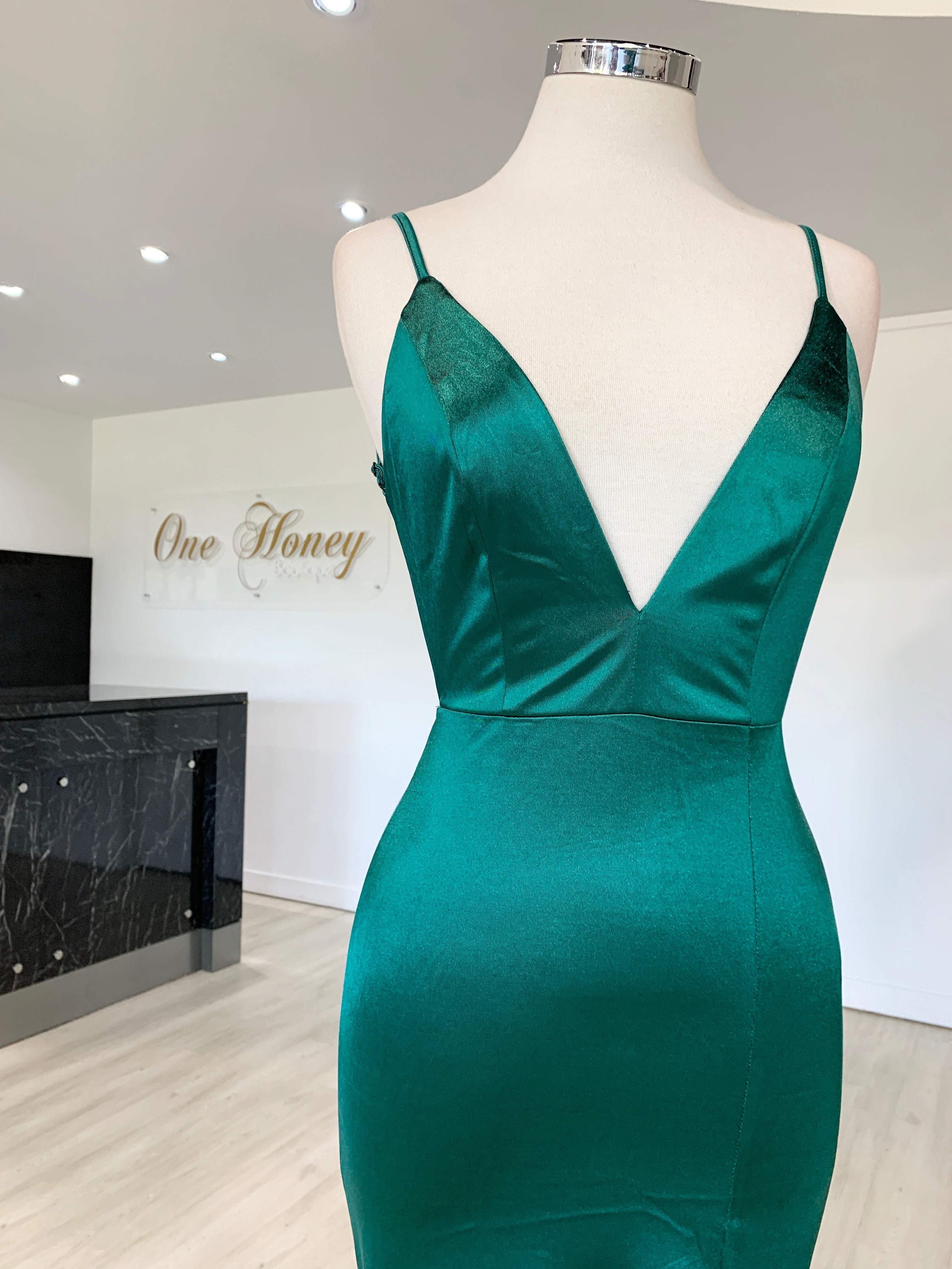 Emerald green low back evening gown displayed on mannequin at One Honey Boutique showroom.