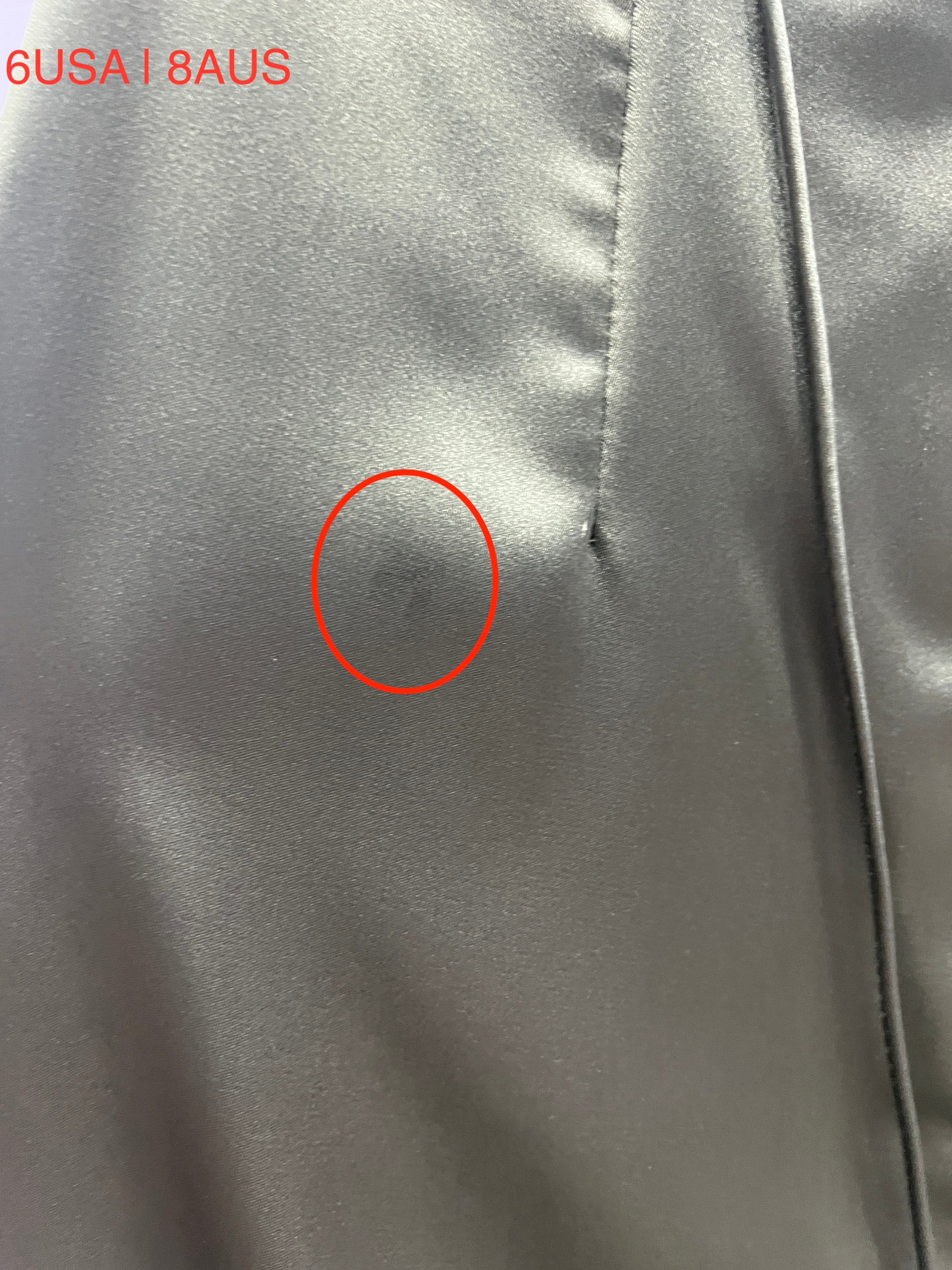 Close-up of imperfection on a satin fabric with a red circle highlighting the flaw. Sizes marked as 6USA and 8AUS.