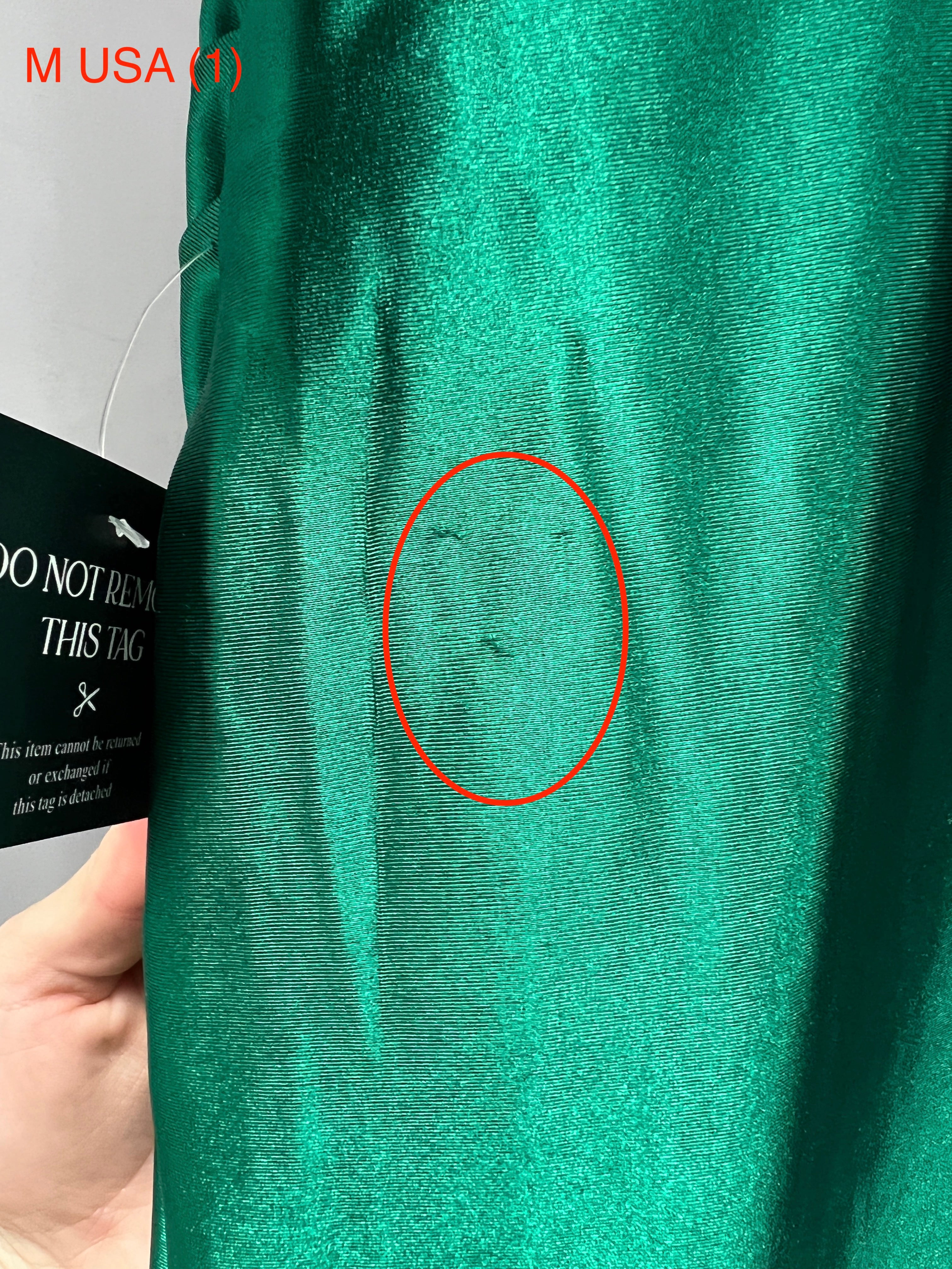 Close-up of the Honey Couture SHARYN Emerald Green dress fabric with a visible flaw, showing silky texture in natural light.