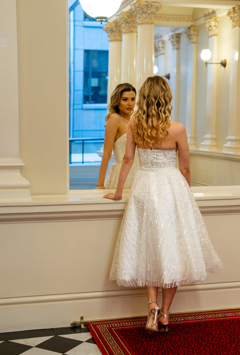 Woman in white strapless sequin and feather midi dress looking at herself in a mirror, inspired by Marilyn Monroe elegance.