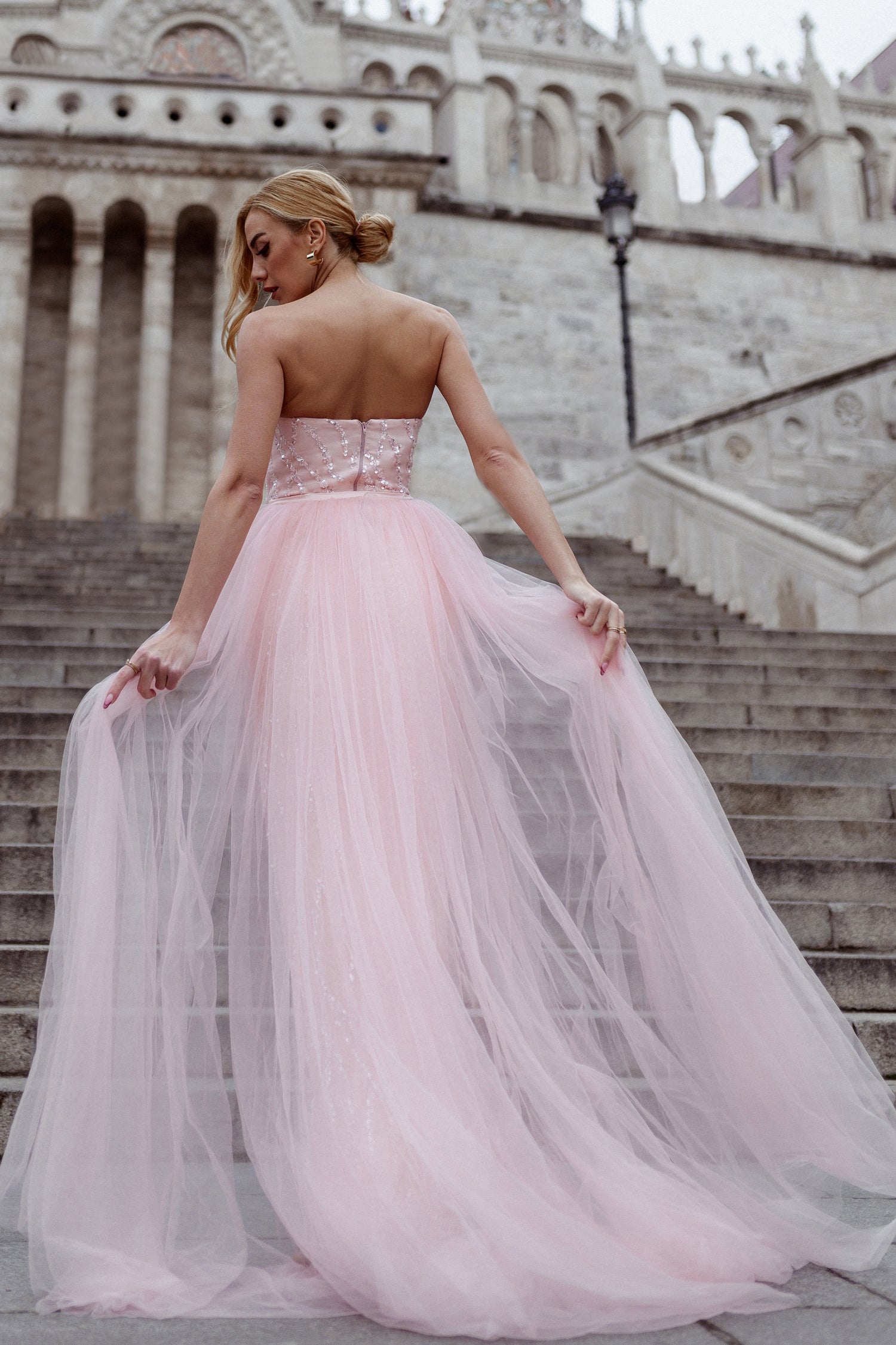 Back view of woman in strapless pink tulle evening gown ascending stone stairs, Brisbane to Gold Coast, Australia.