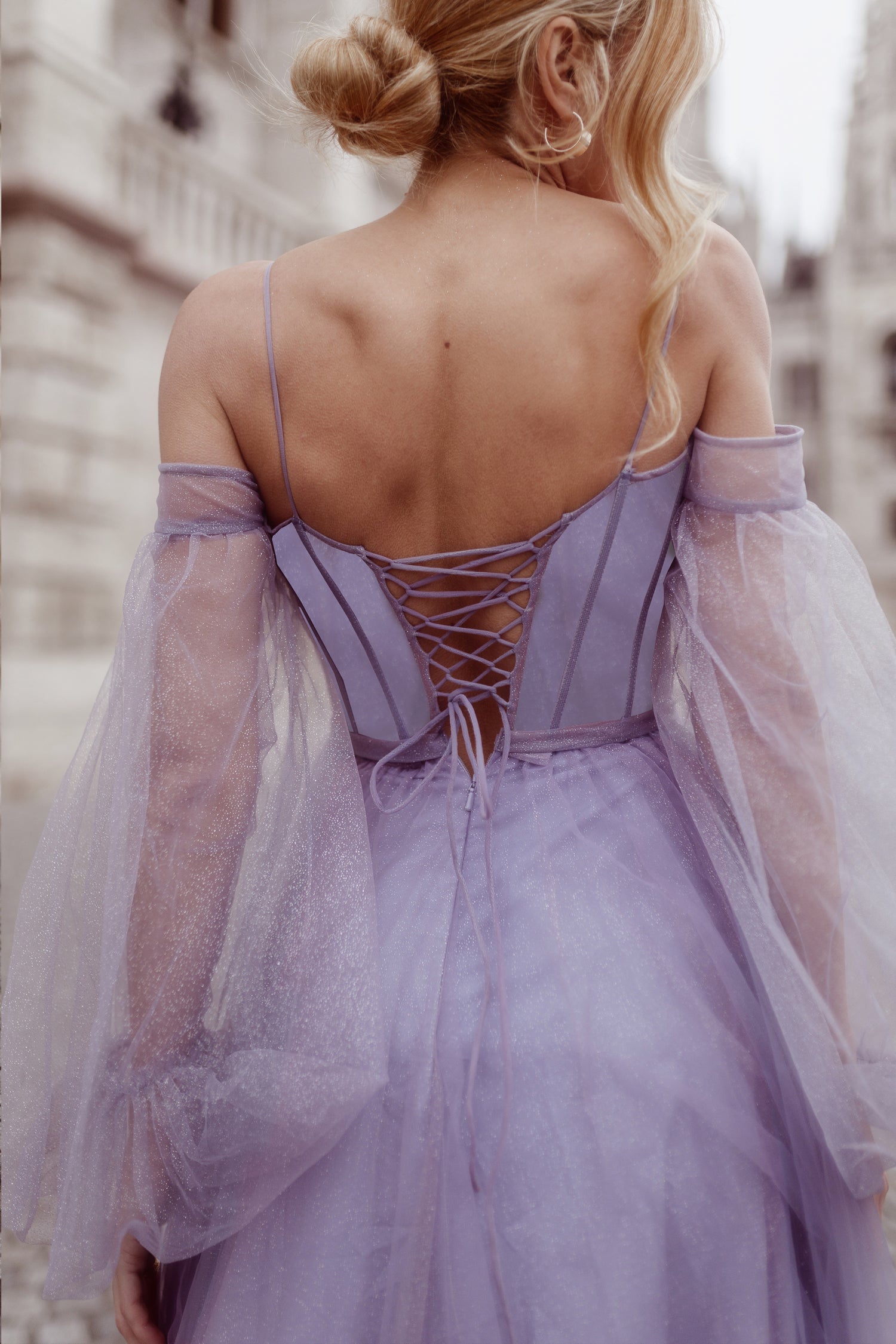 Back view of a lavender ball gown with sheer off-the-shoulder sleeves and lace-up corset detail, perfect for a formal event.