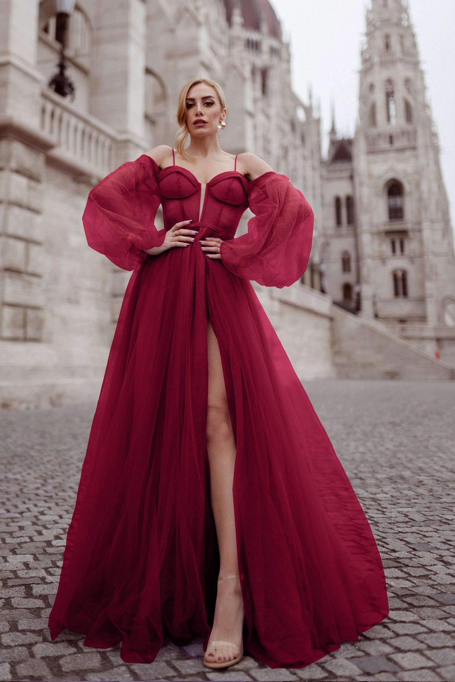 Elegant red ball gown with puffed sleeves and sweetheart neckline, perfect for formal events, photographed in front of a historic building.