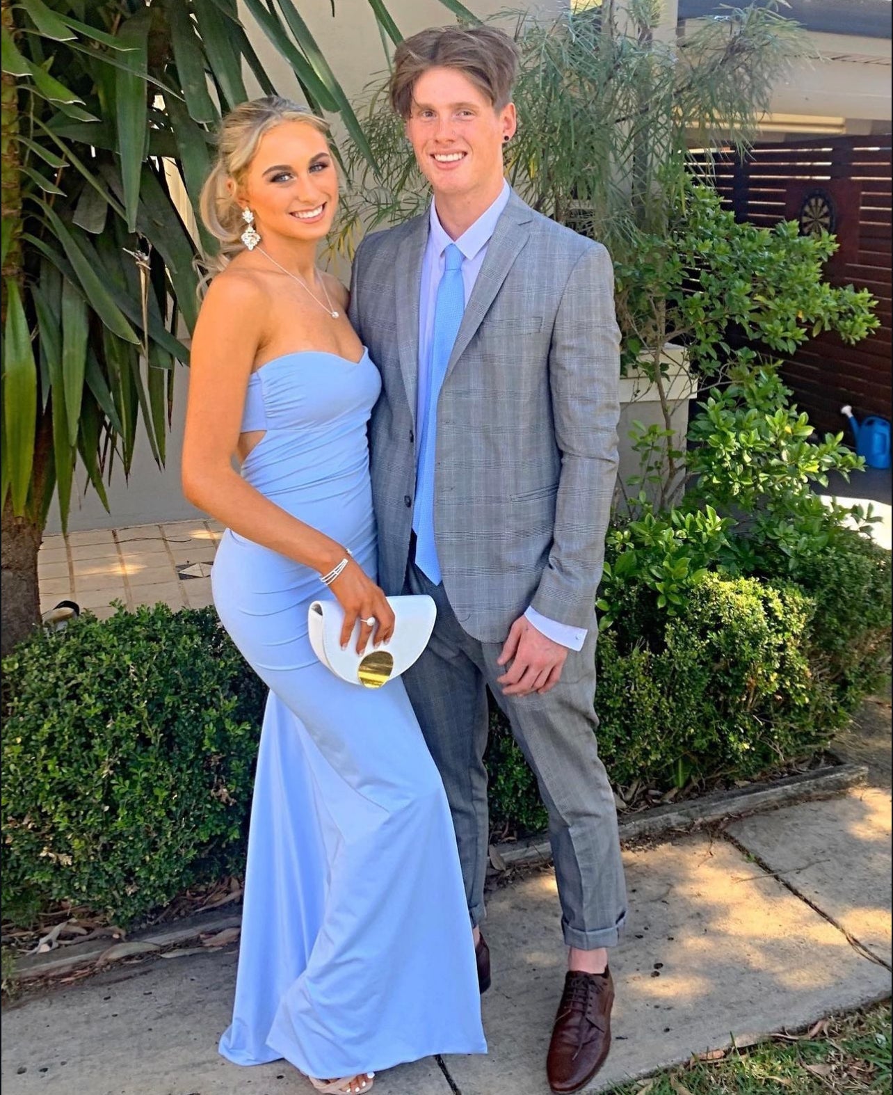 Woman in blue strapless formal gown with sweetheart neckline standing next to a man in a gray suit outdoors.