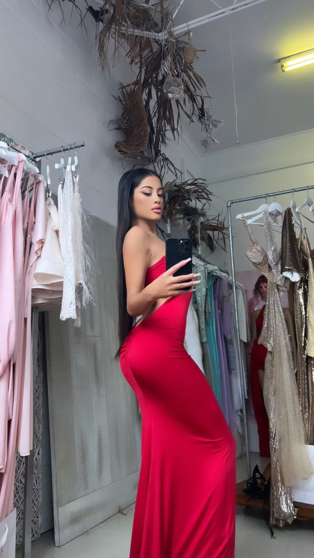 Woman wearing a red strapless mermaid dress in a boutique setting.