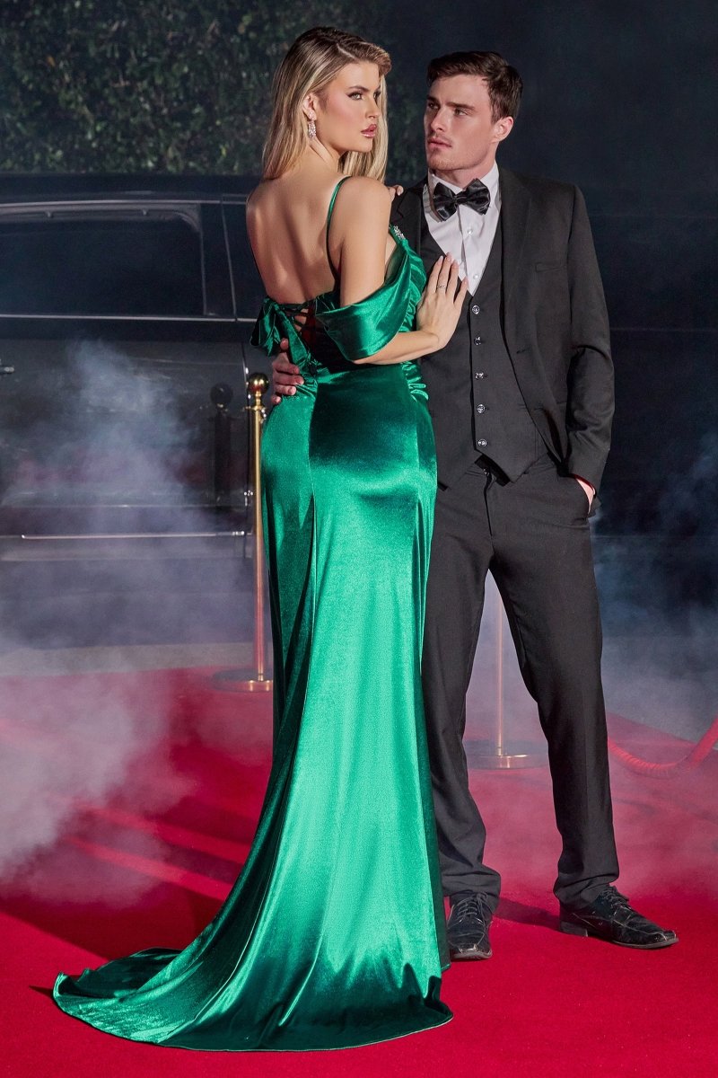 Elegant woman in a green satin evening gown with a low back, standing on a red carpet with a man in a black tuxedo, surrounded by smoke.