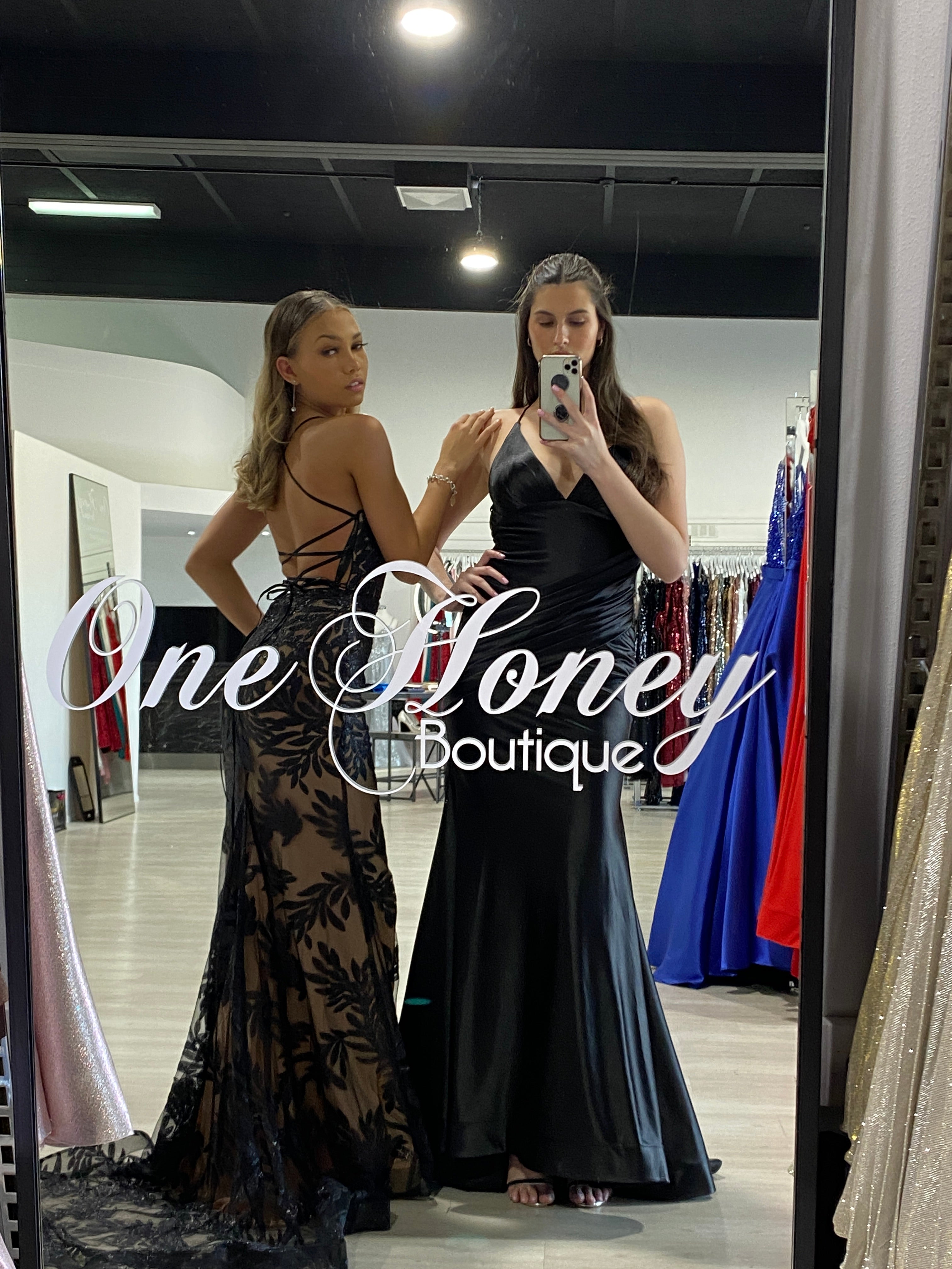 Two women in elegant formal gowns with lace detailing and deep V-neck, inside One Honey Boutique, Brisbane to Gold Coast.