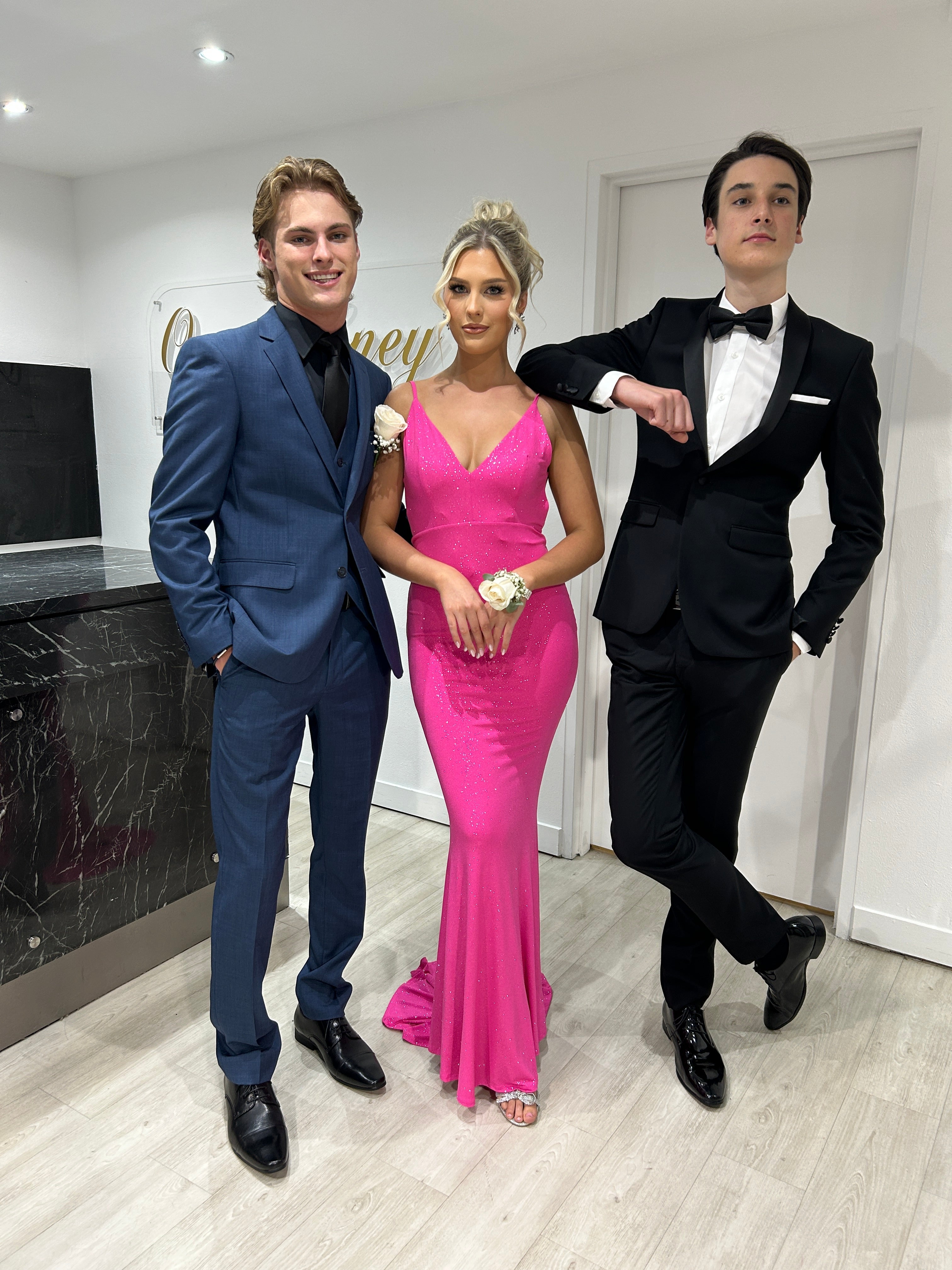 SKY mermaid formal dress in pink with glitter finish, worn by a woman between two men in suits. Evening gown Brisbane to Gold Coast.