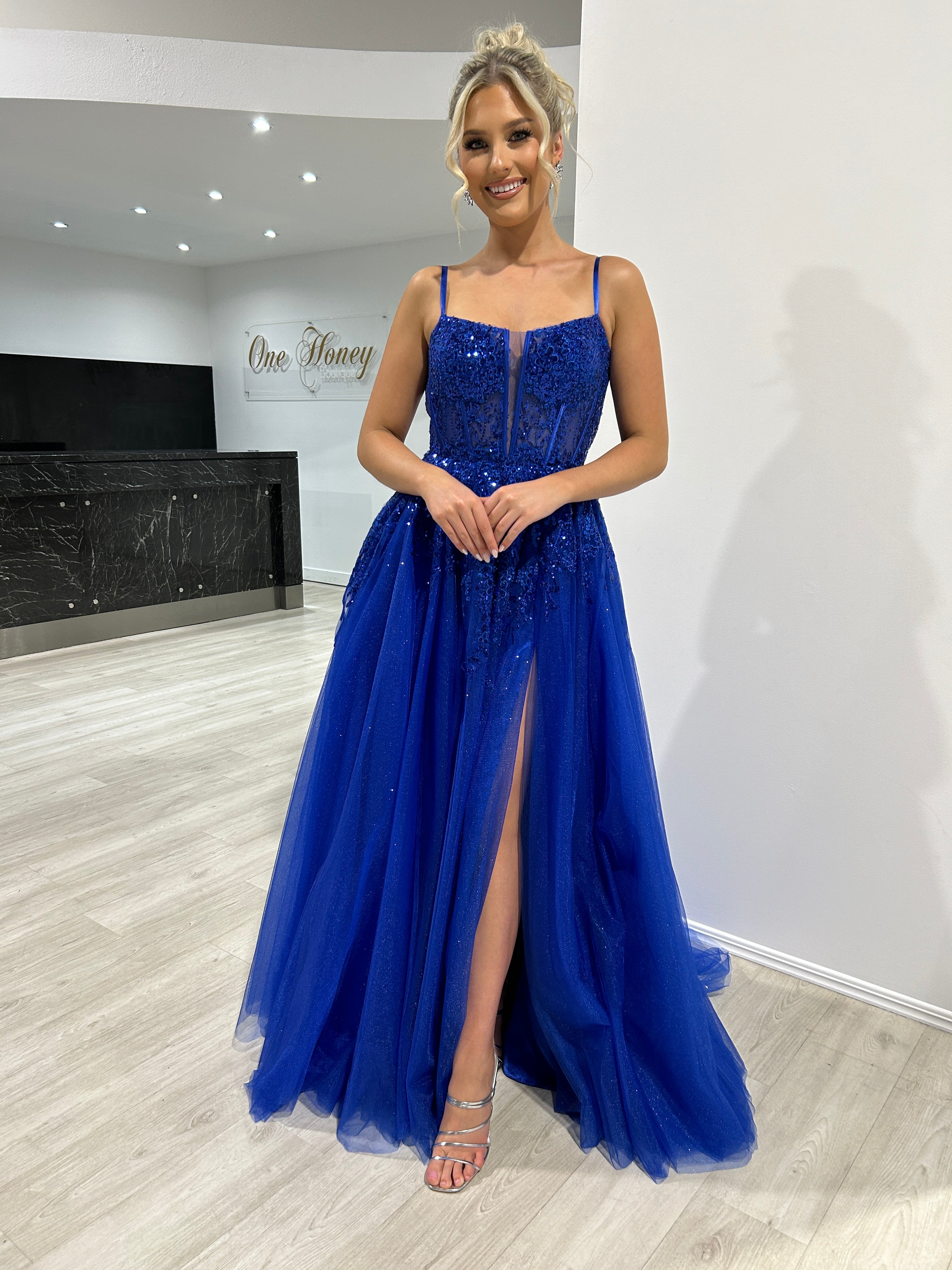 Woman in a blue tulle evening gown with lace details, standing in a modern room, embodying elegance for prom or formal events.