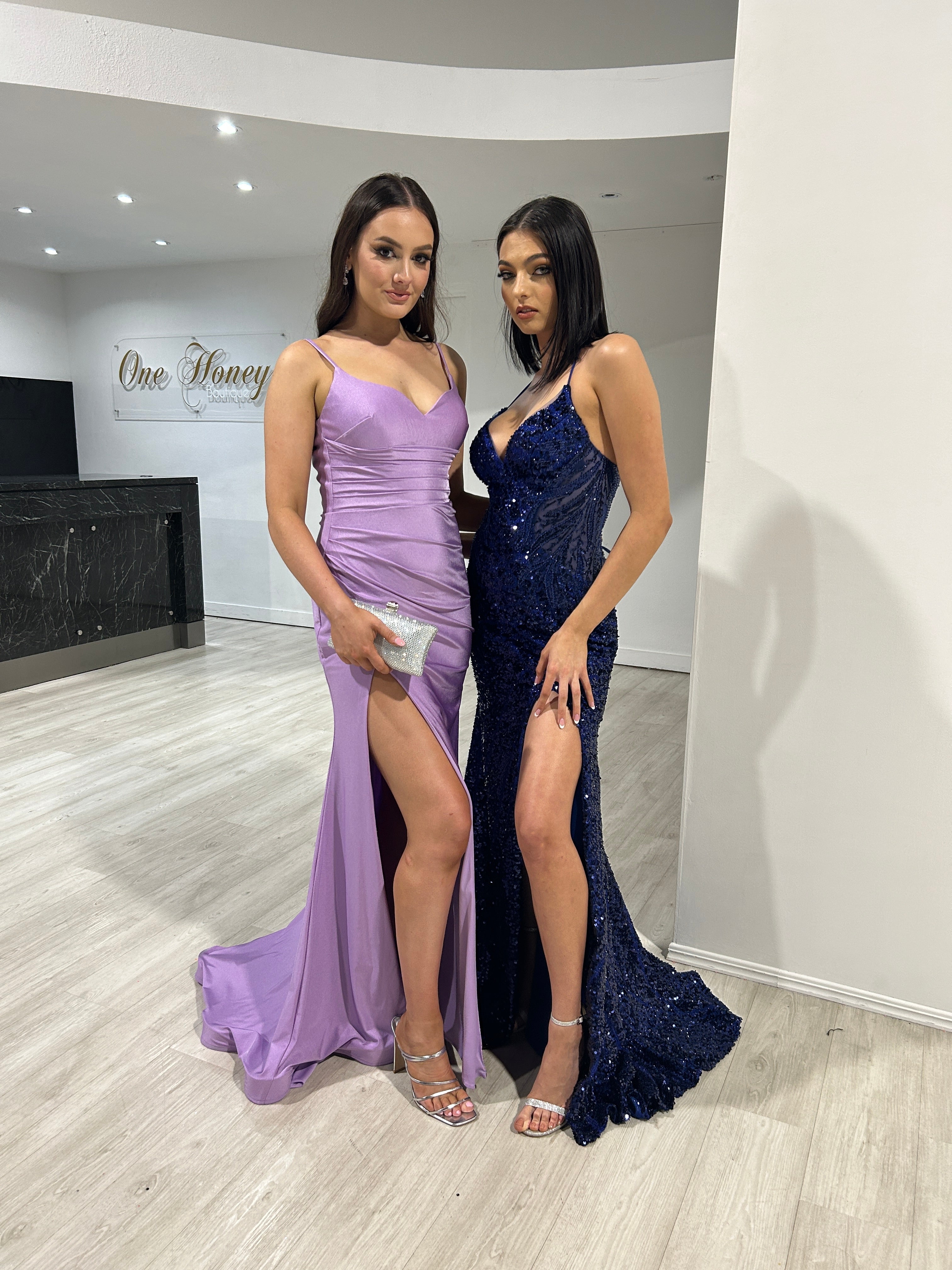 Two women in elegant evening gowns, one in lavender with a slit and the other in navy sequin with a mermaid silhouette, Brisbane to Gold Coast.
