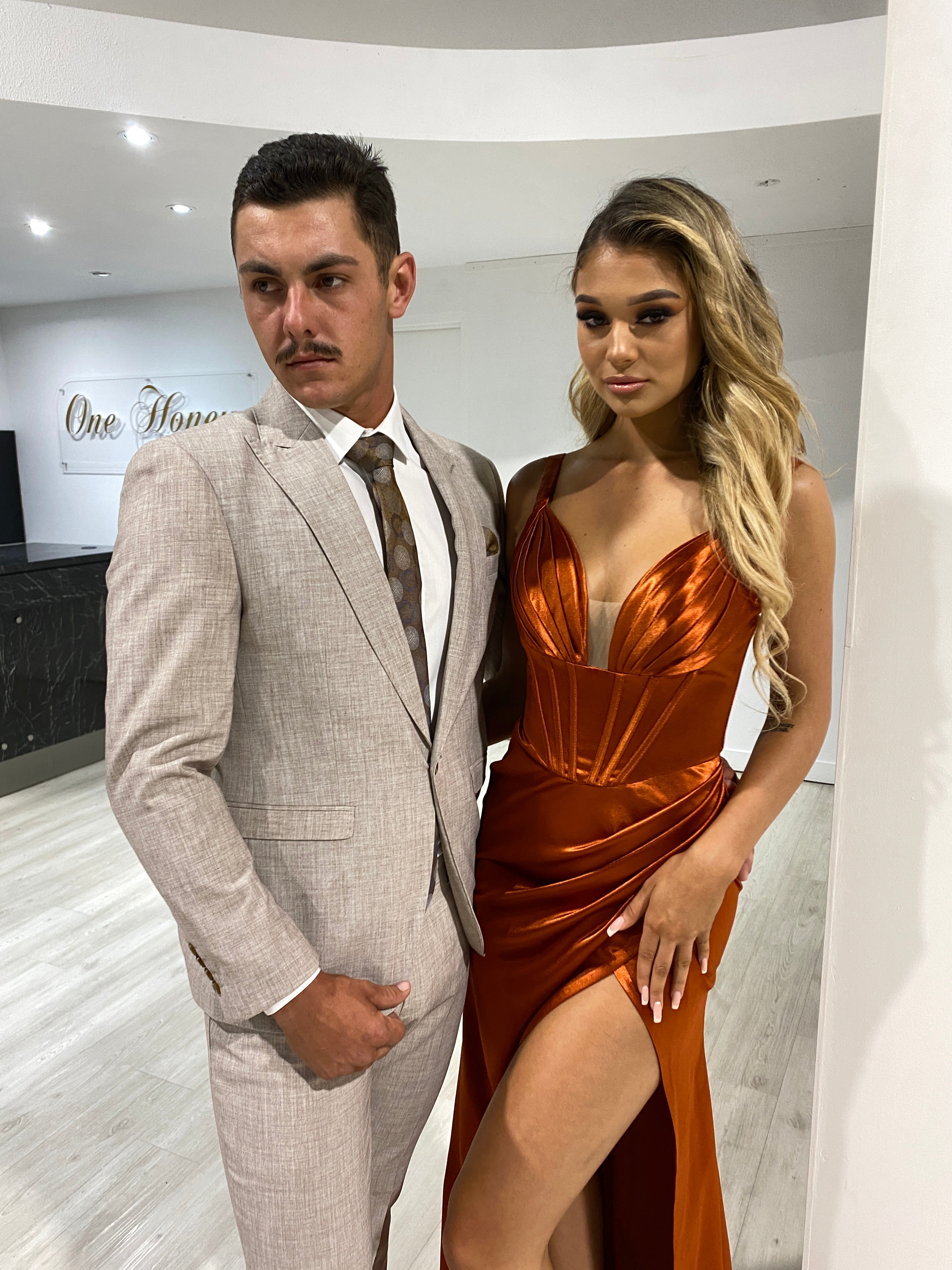 A couple dressed in formal attire; the woman wears a silky satin corset bustier dress with a leg split, and the man in a light suit jacket. Brisbane to Gold Coast, Australia.