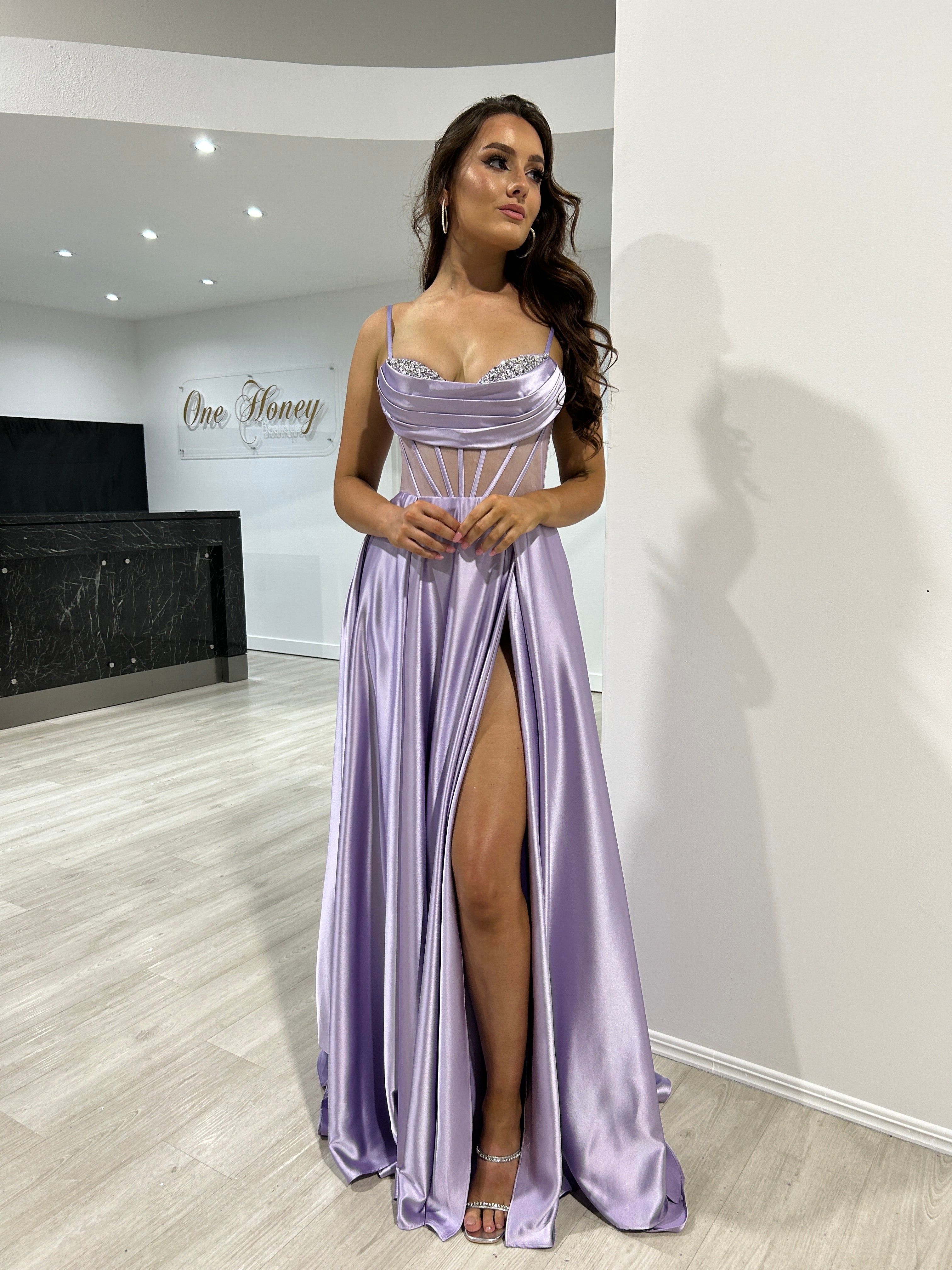 Lilac satin evening gown with pleated cowl neckline and side slit, featuring diamanté bust detail, modeled indoors. Elegant formal wear.