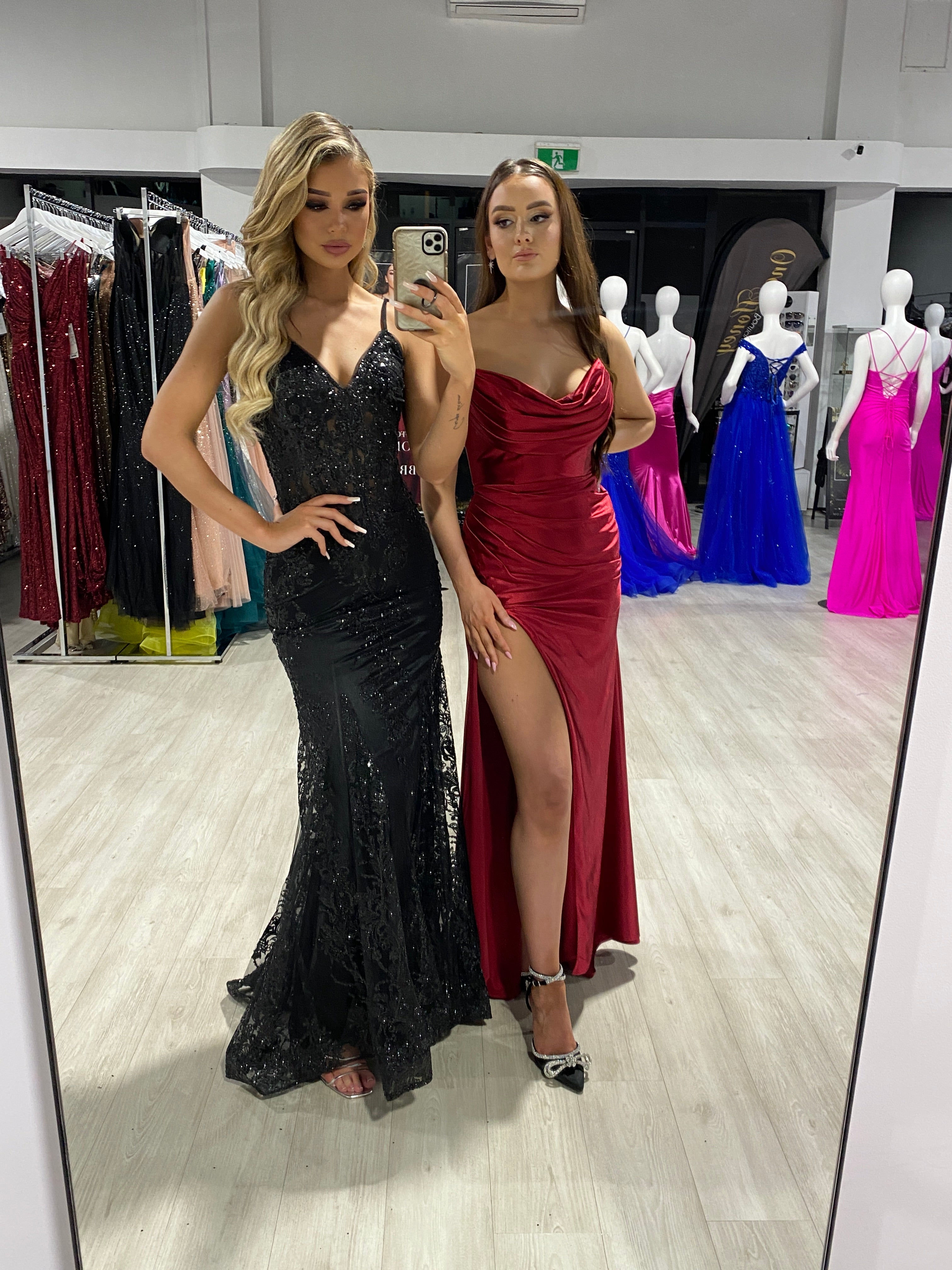 Women in a chic boutique modeling a black sequin evening gown and a red satin slit formal dress. Fashion display in Brisbane to Gold Coast.