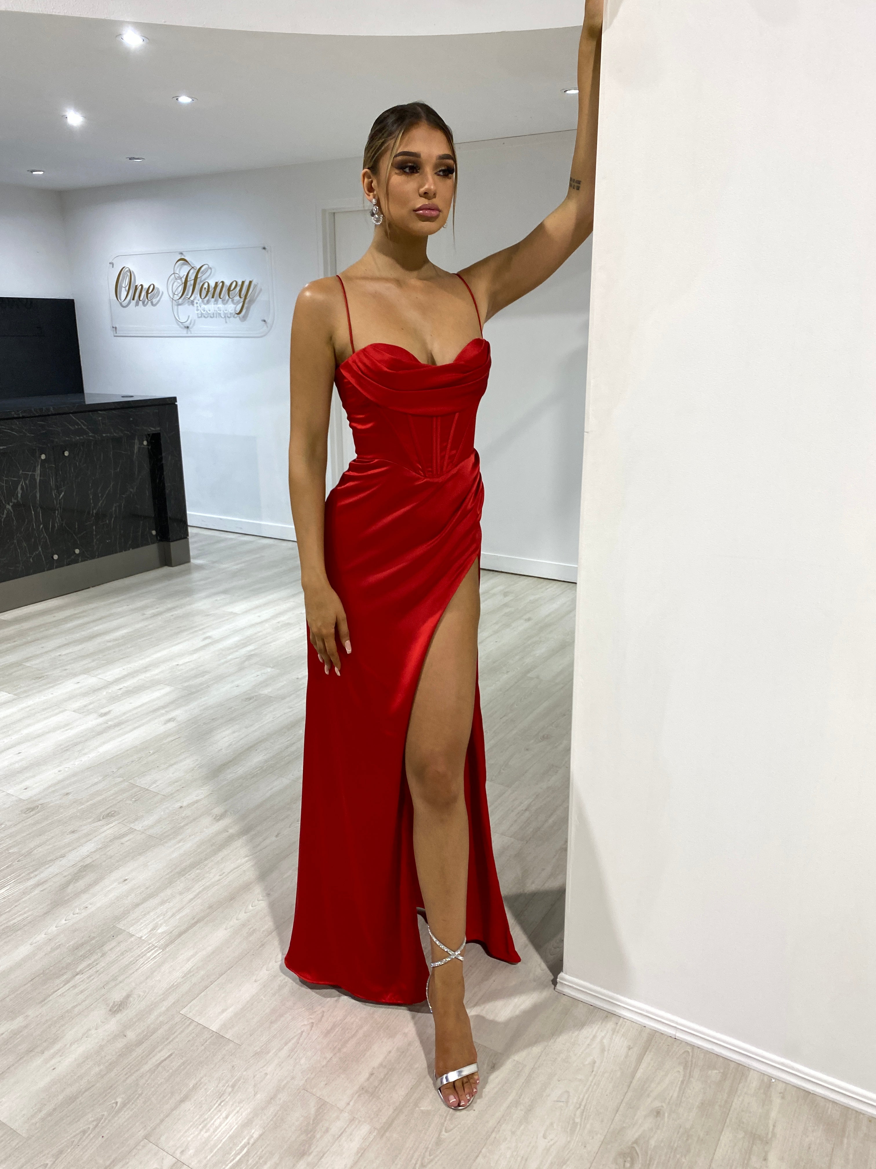 Woman wearing Honey Couture ZENDAYA red satin corset bustier gown, featuring leg split and lace up back. Perfect for prom, evening events.