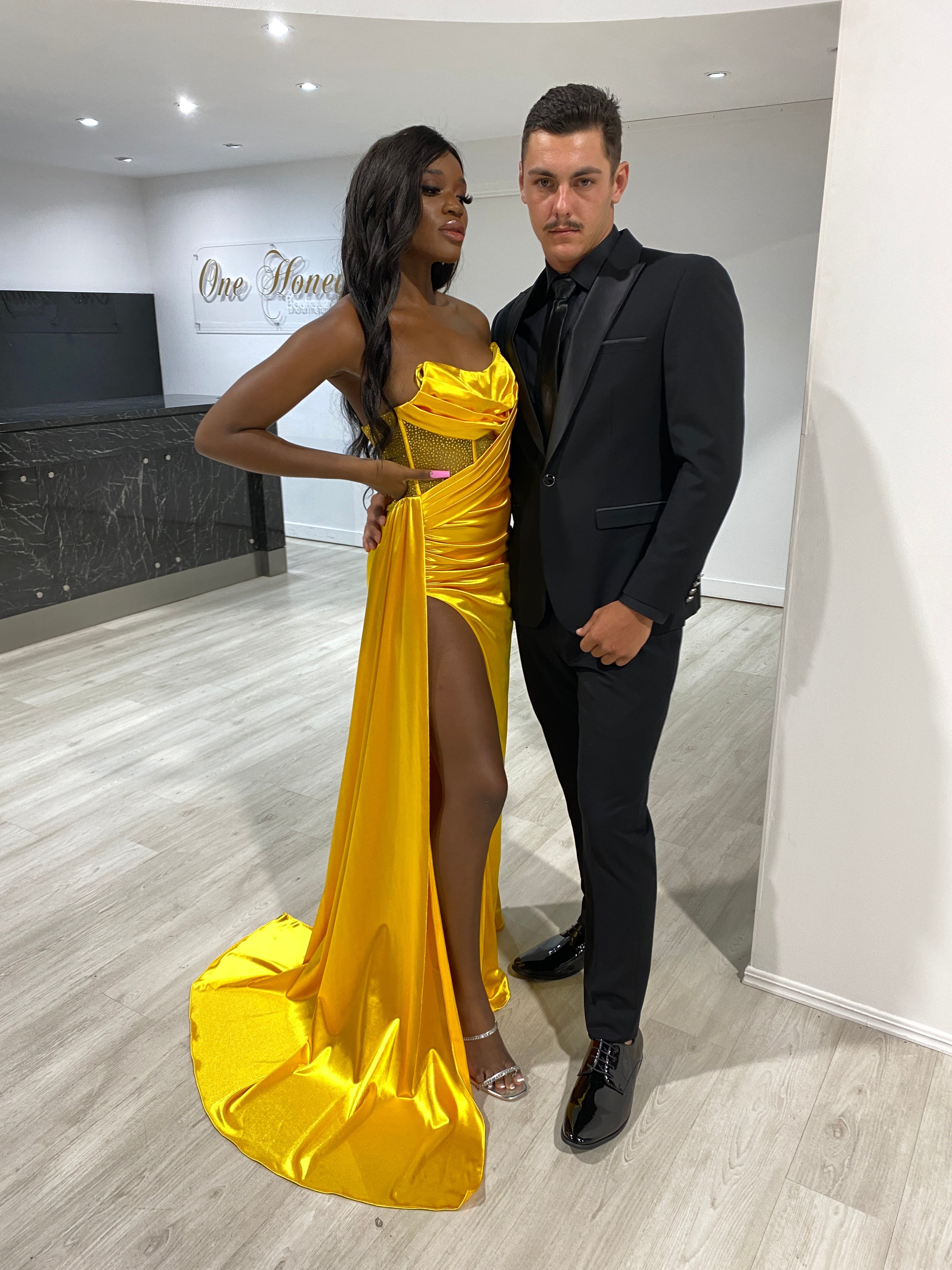 Golden satin evening gown with high slit, paired with a black tuxedo. Stylish formal wear for events from Brisbane to Gold Coast, Australia.