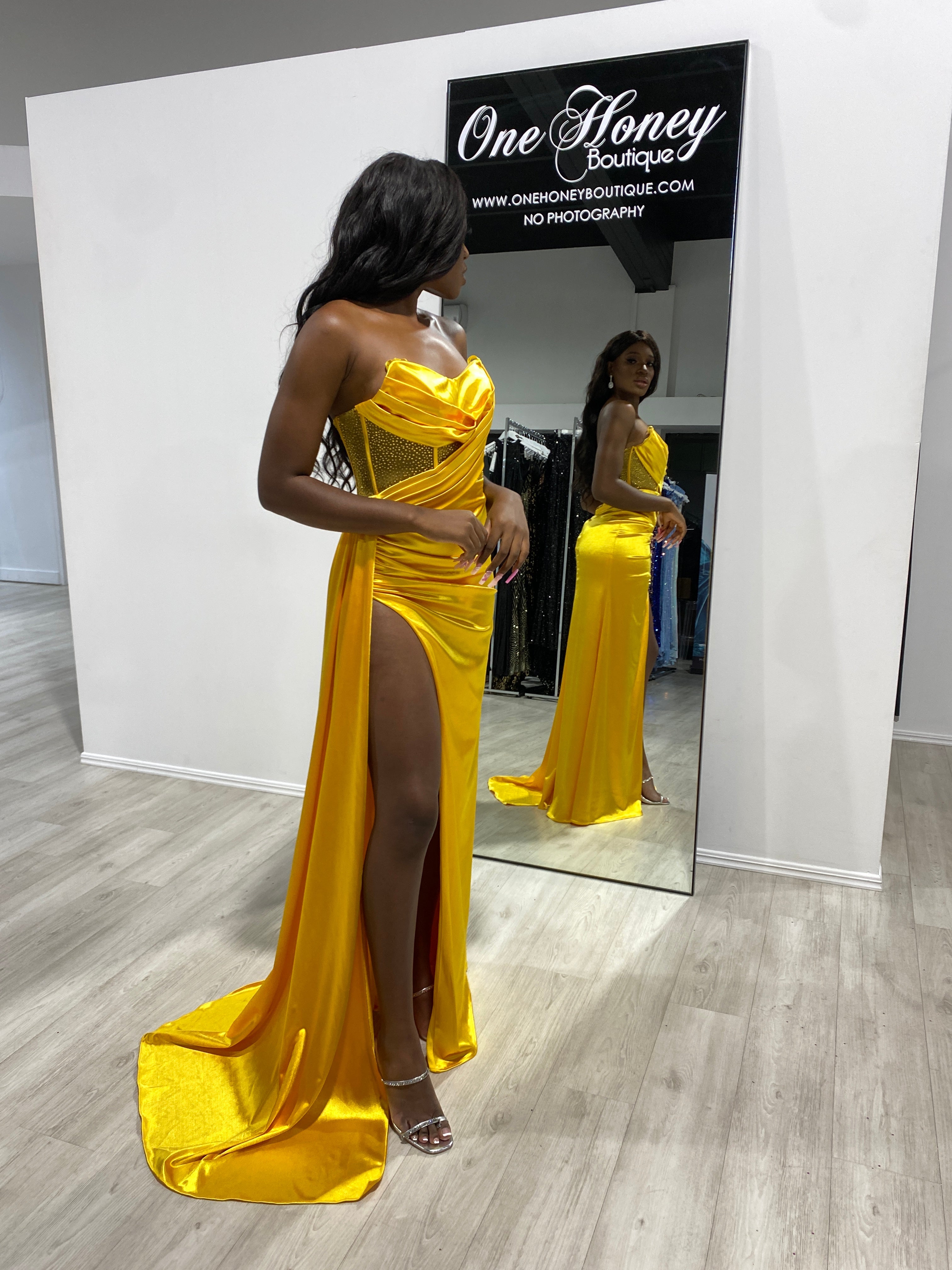 Woman in a vibrant yellow satin gown with a sculpted bodice and high slit, reflected in a boutique mirror. Brisbane to Gold Coast.