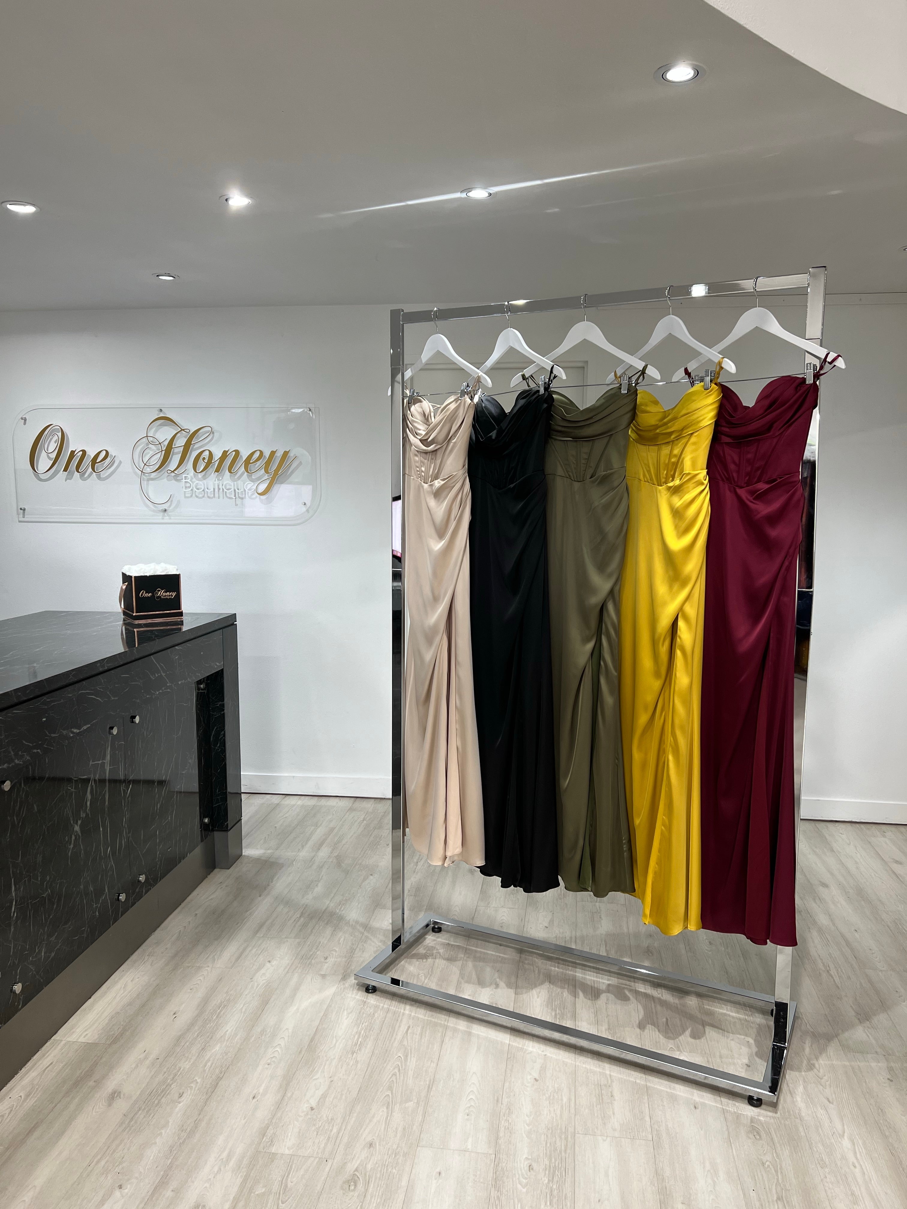 Elegant satin dresses in various colors, including a sage corset gown with leg slit, displayed on a rack. Perfect for formal events. Brisbane to Gold Coast.