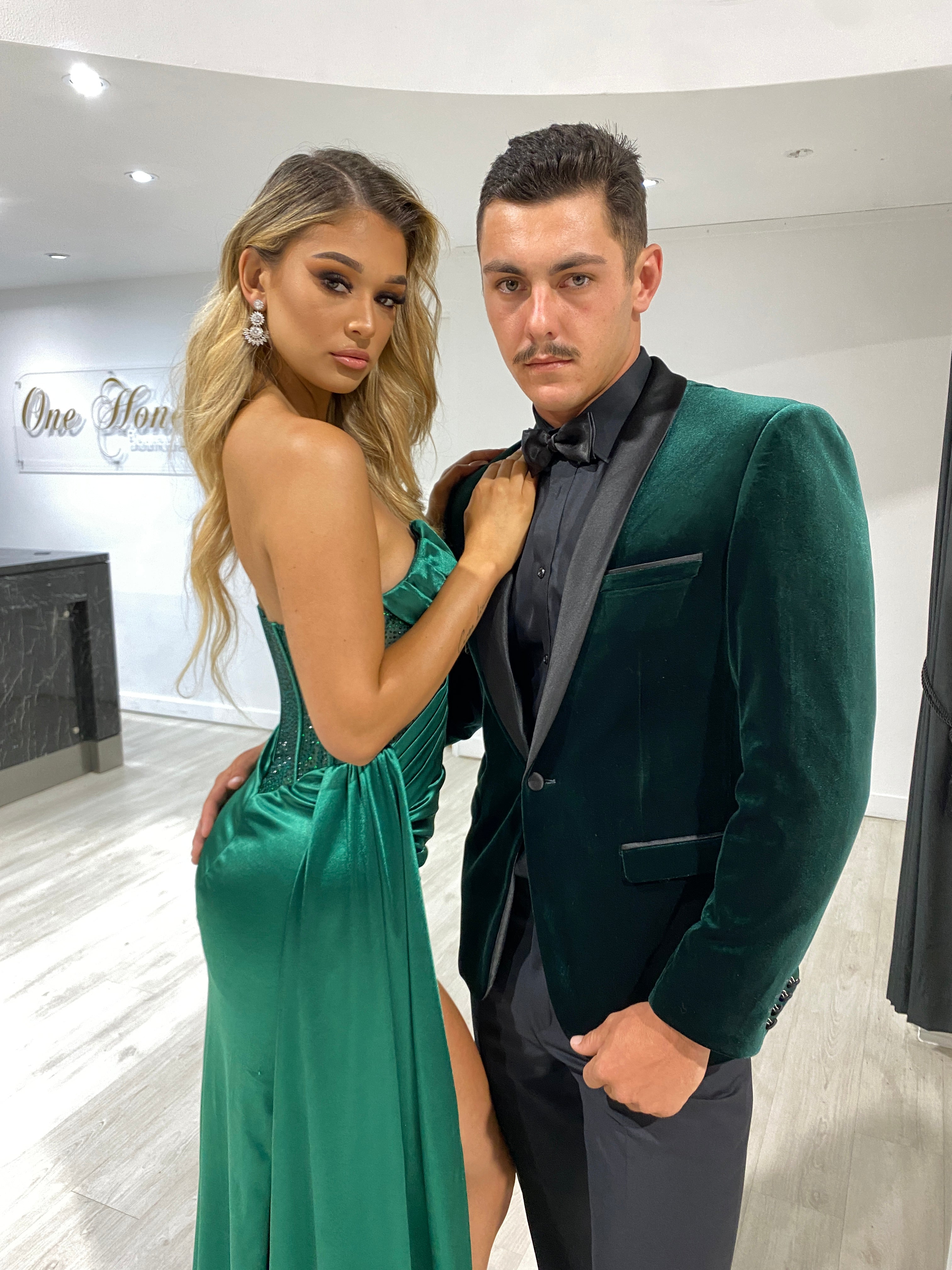 Couple in matching green formal attire; woman in strapless gown with slit, man in green velvet blazer. Brisbane to Gold Coast