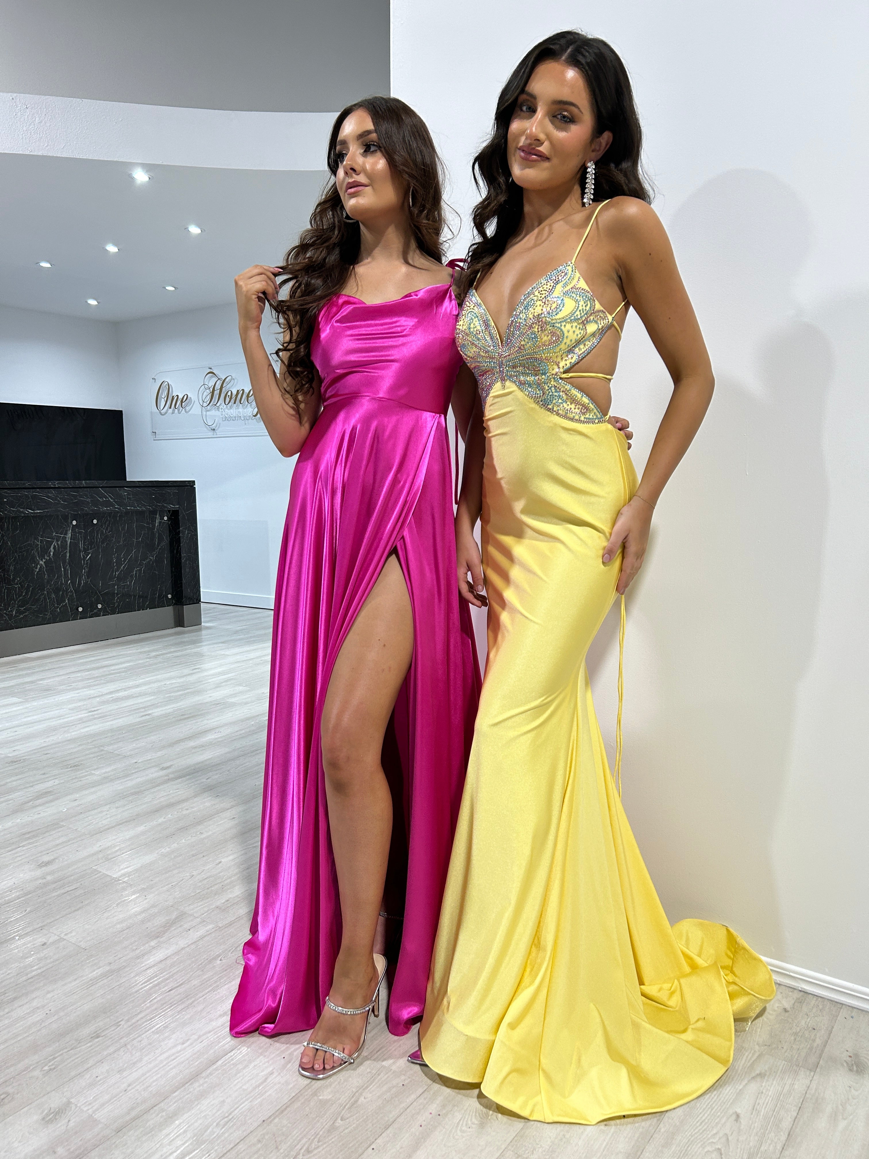 Two women in vibrant pink and yellow formal gowns, featuring a satin slit and glitter bodice. Stylish evening wear. Brisbane to Gold Coast.