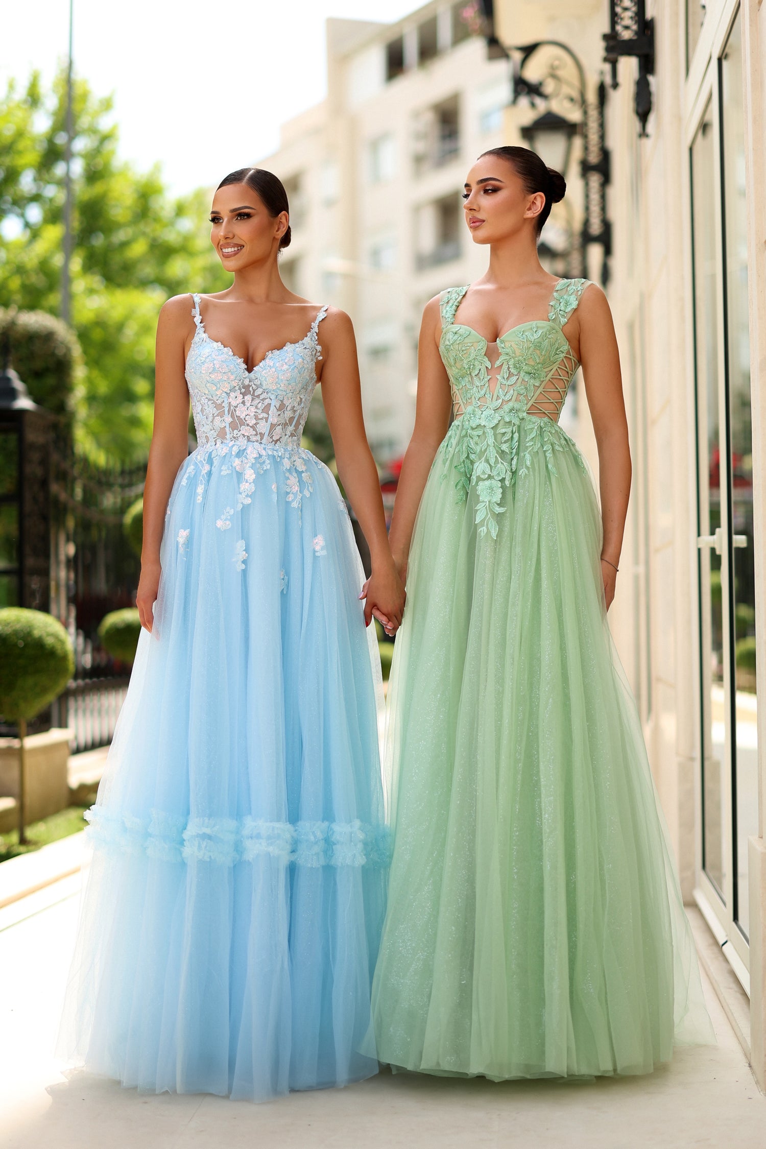 Two women in elegant lace corset prom gowns, one blue and one green, standing outdoors. Perfect for formal events. Brisbane to Gold Coast.