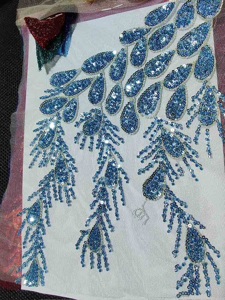 Intricate blue crystal beading on fabric for luxury gown design, featuring teardrop and fringe patterns, ideal for evening wear.
