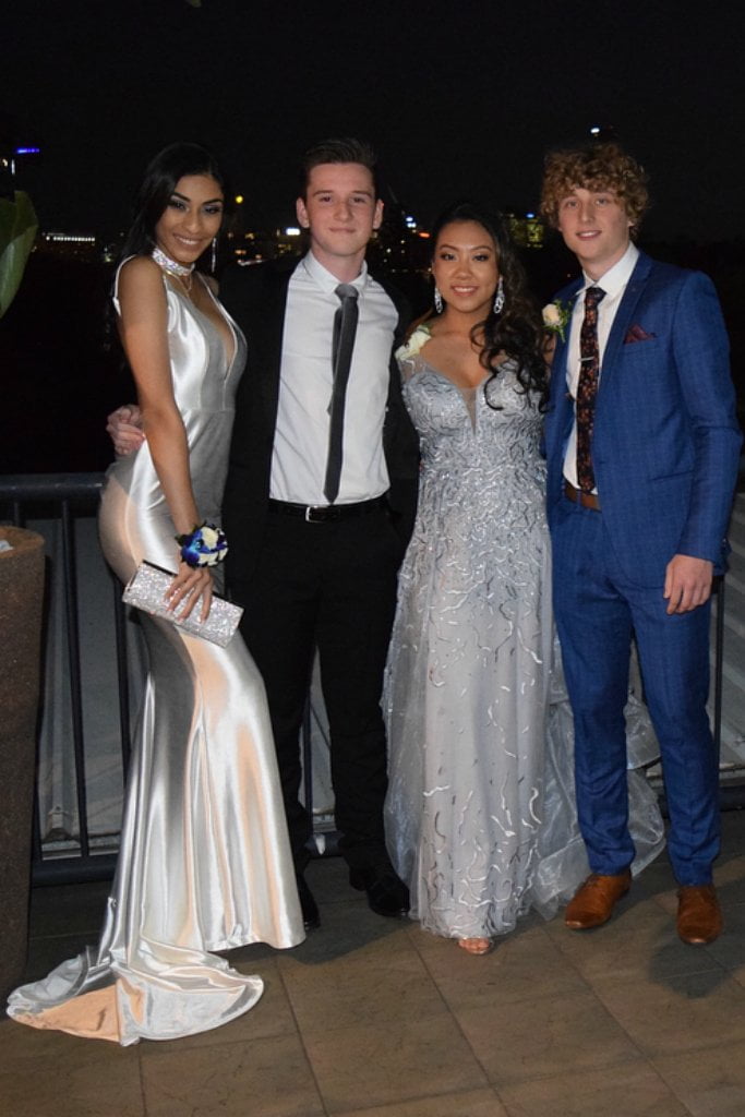 Group of four young adults dressed in formal evening attire standing outdoors at night.