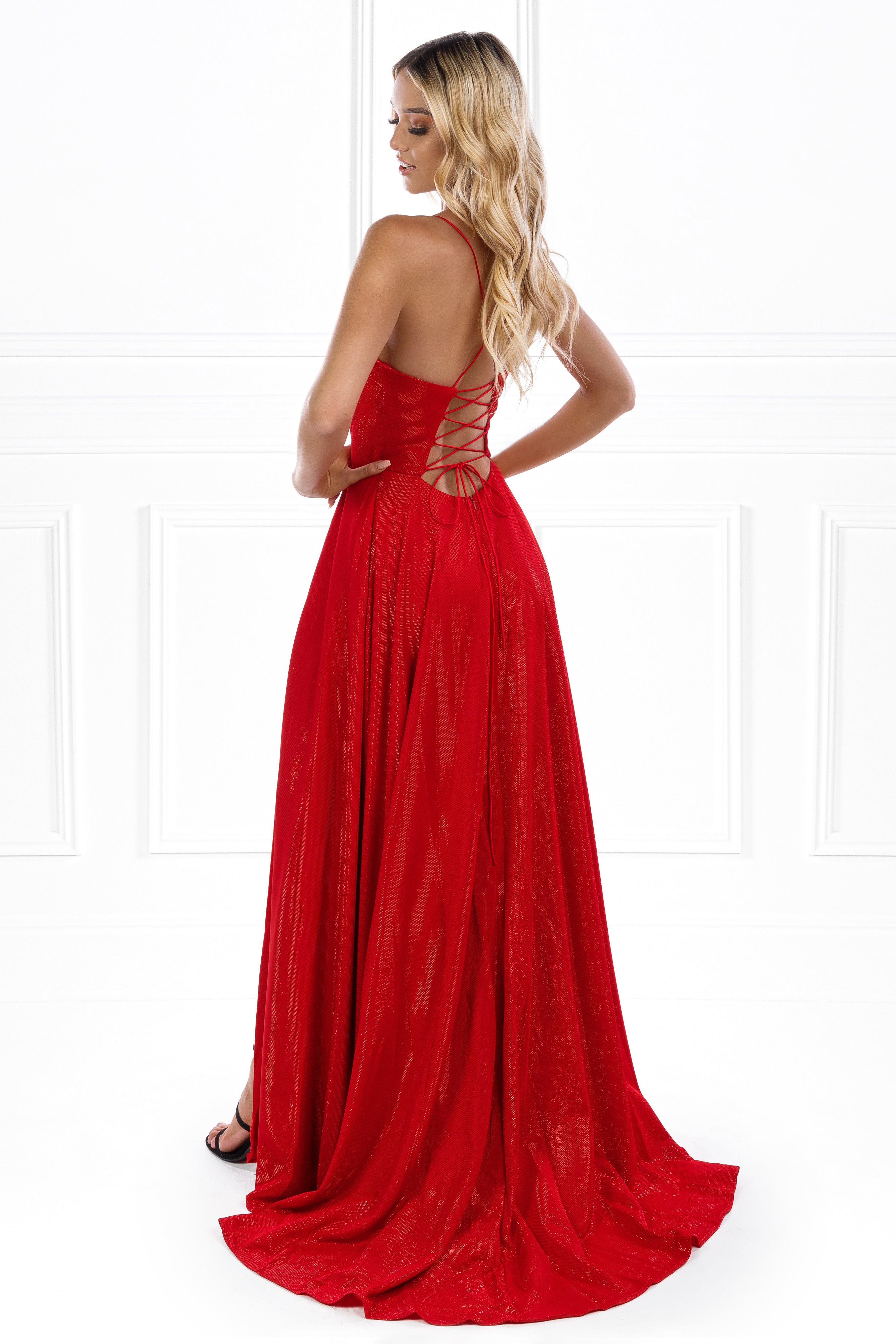 Woman wearing Honey Couture KYLA red shimmer gown with lace-up back, showcasing elegant leg split. Perfect for formal occasions. Australian designer.