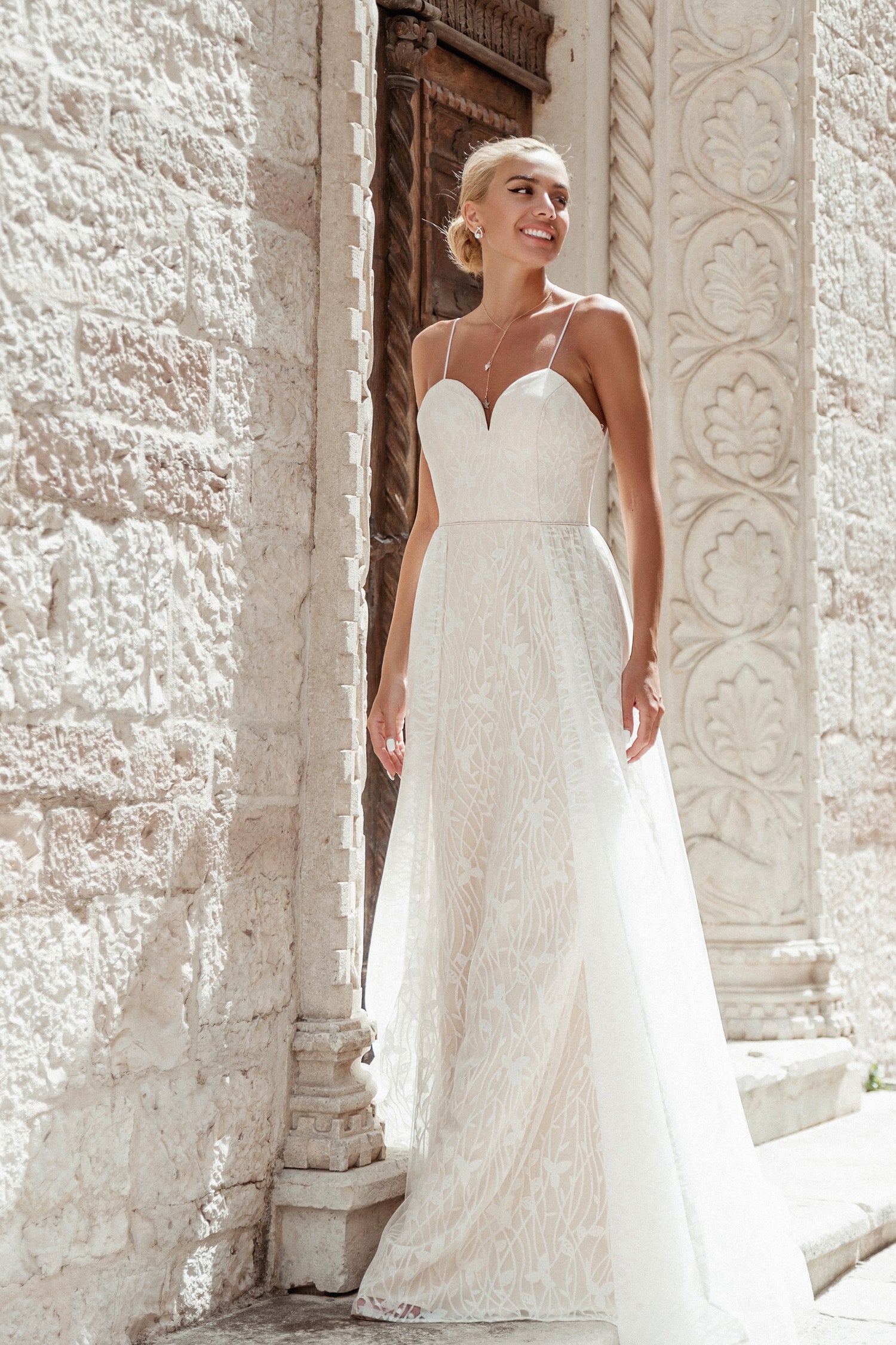 Elegant white lace wedding gown with sweetheart neckline, featured in an outdoor architectural setting.