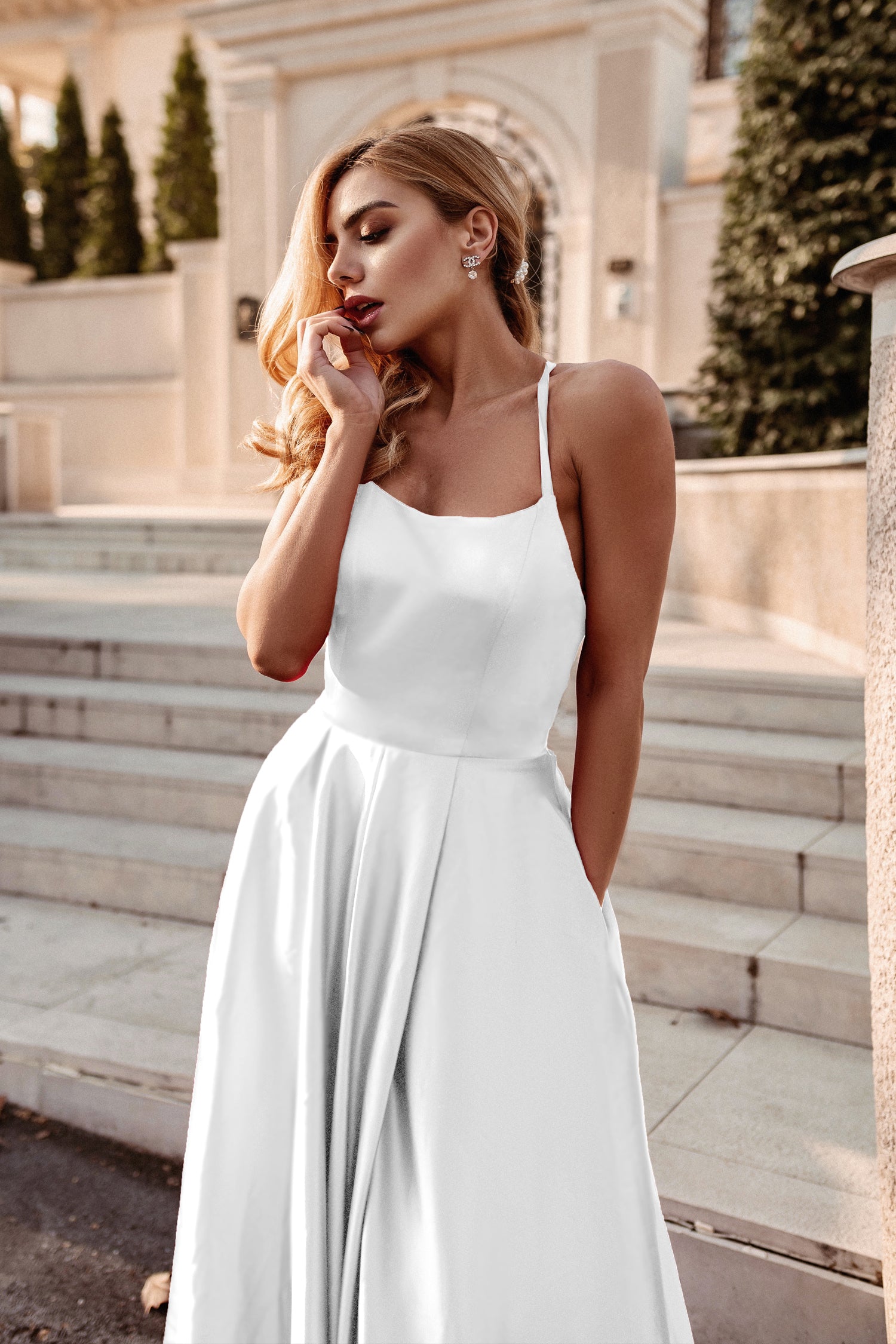 Elegant woman in a white satin gown with a square neckline, photographed outdoors on elegant stone steps.