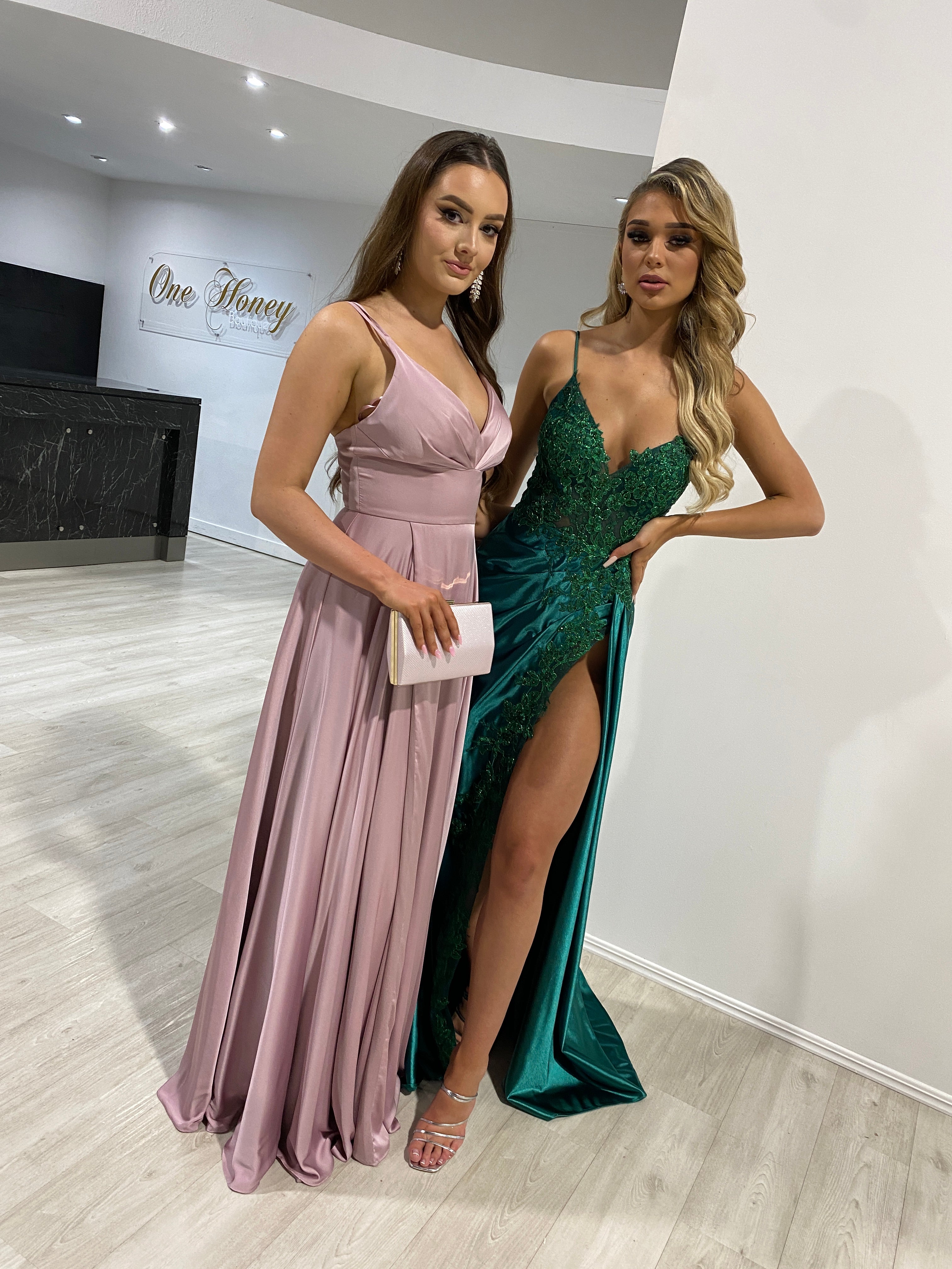 Two women in elegant A-line dresses; one with a satin V-neck and pleated bust, the other with a deep V-neck and leg slit. Brisbane to Gold Coast.