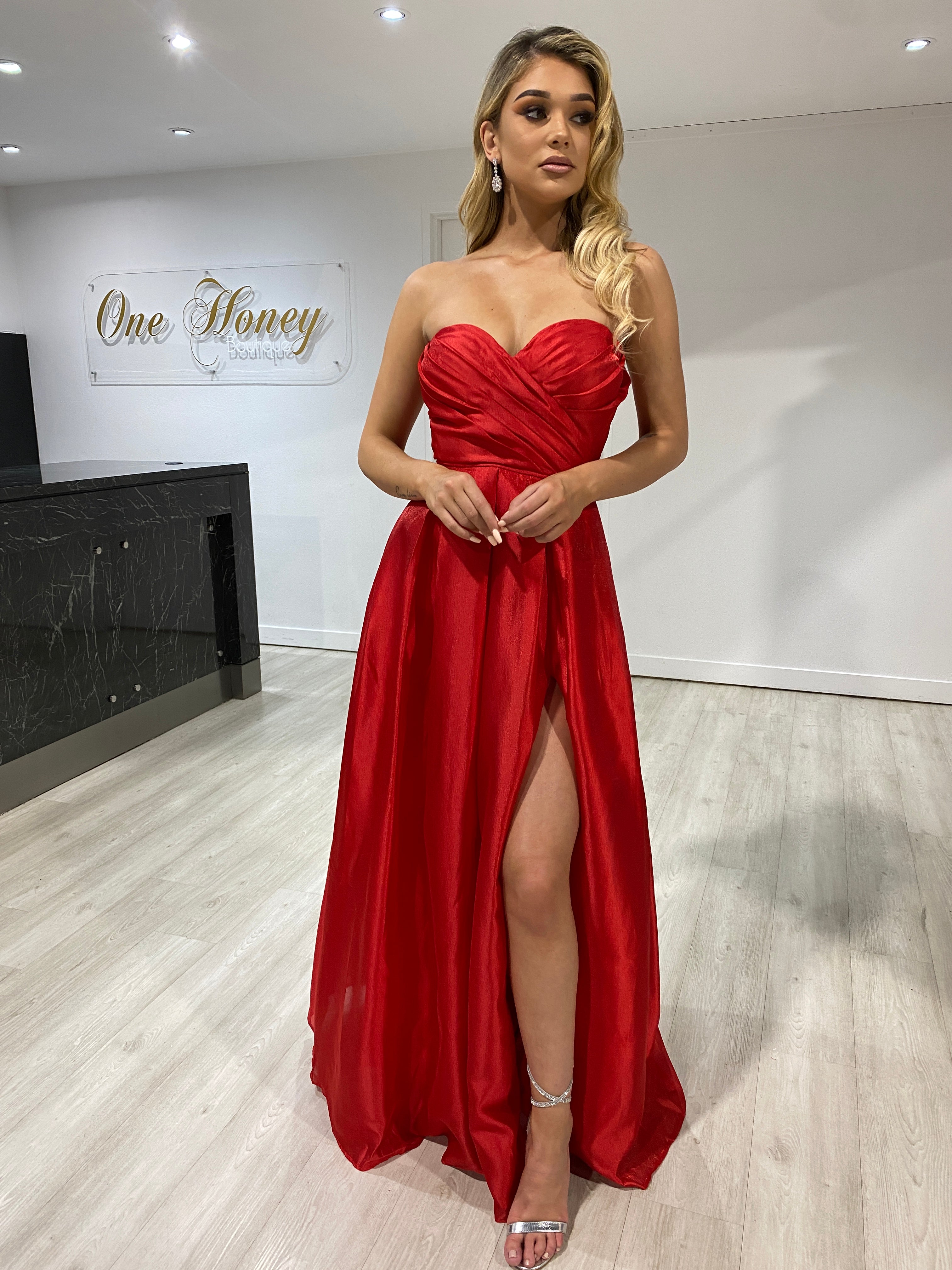Woman in Honey Couture RUBY red strapless ballgown with leg split, posing indoors. Australian designer prom and evening gown.