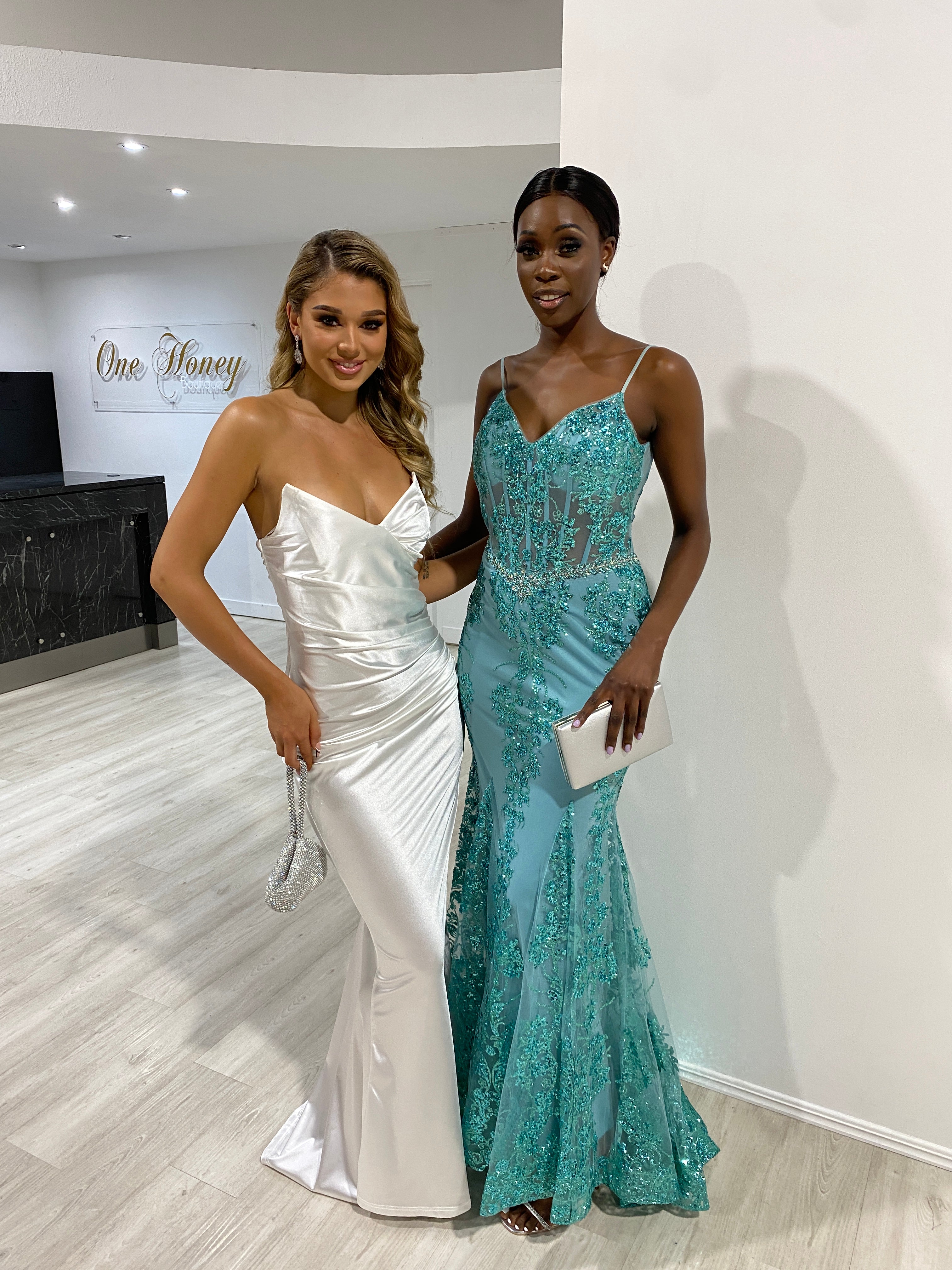Two women posing in Honey Couture dresses: white satin strapless gown and turquoise lace evening gown. Australian designer prom dresses.