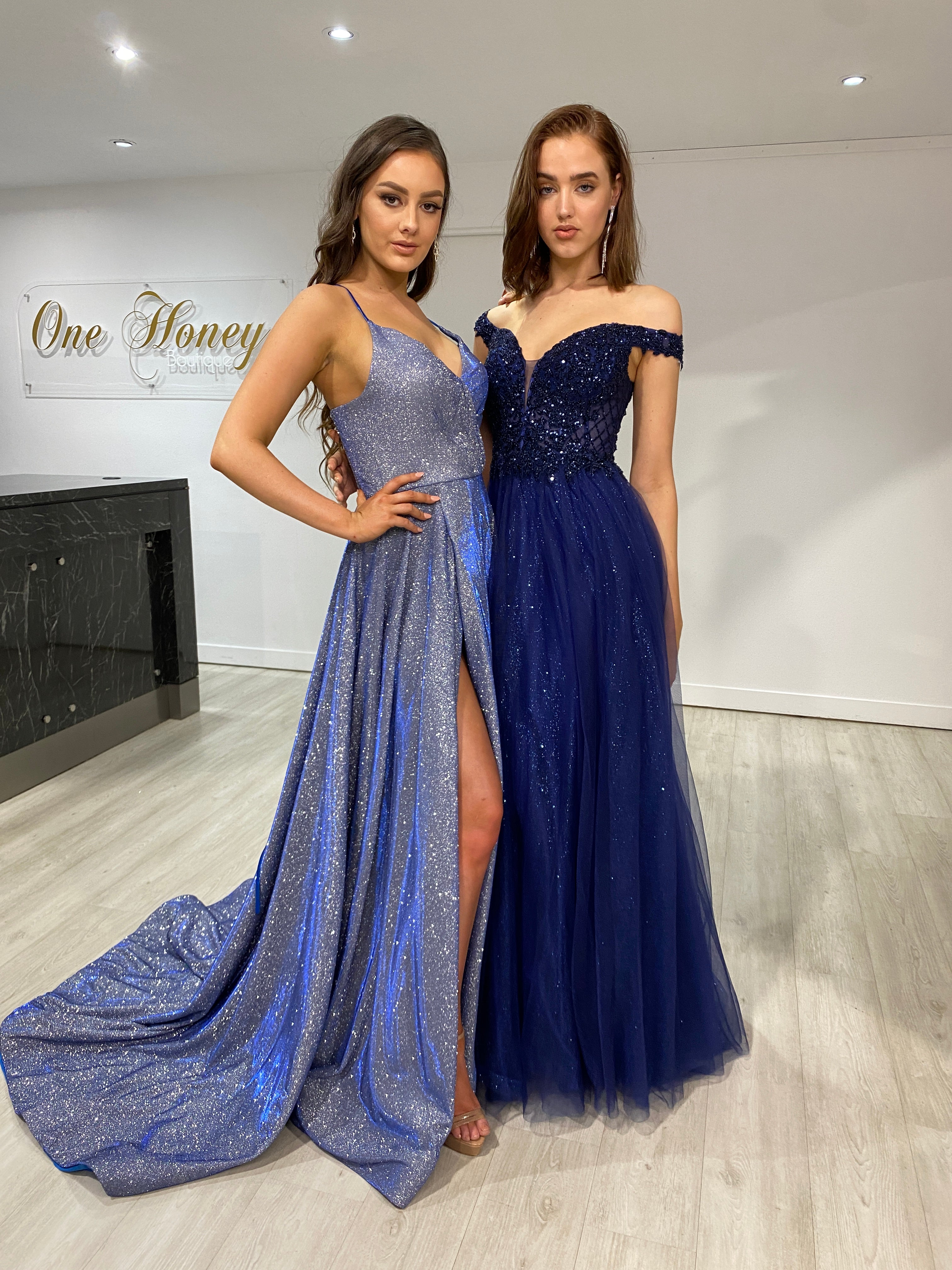 Two women in elegant Honey Couture formal gowns stand in a stylish boutique, showcasing Australian designer prom dresses and evening gowns.