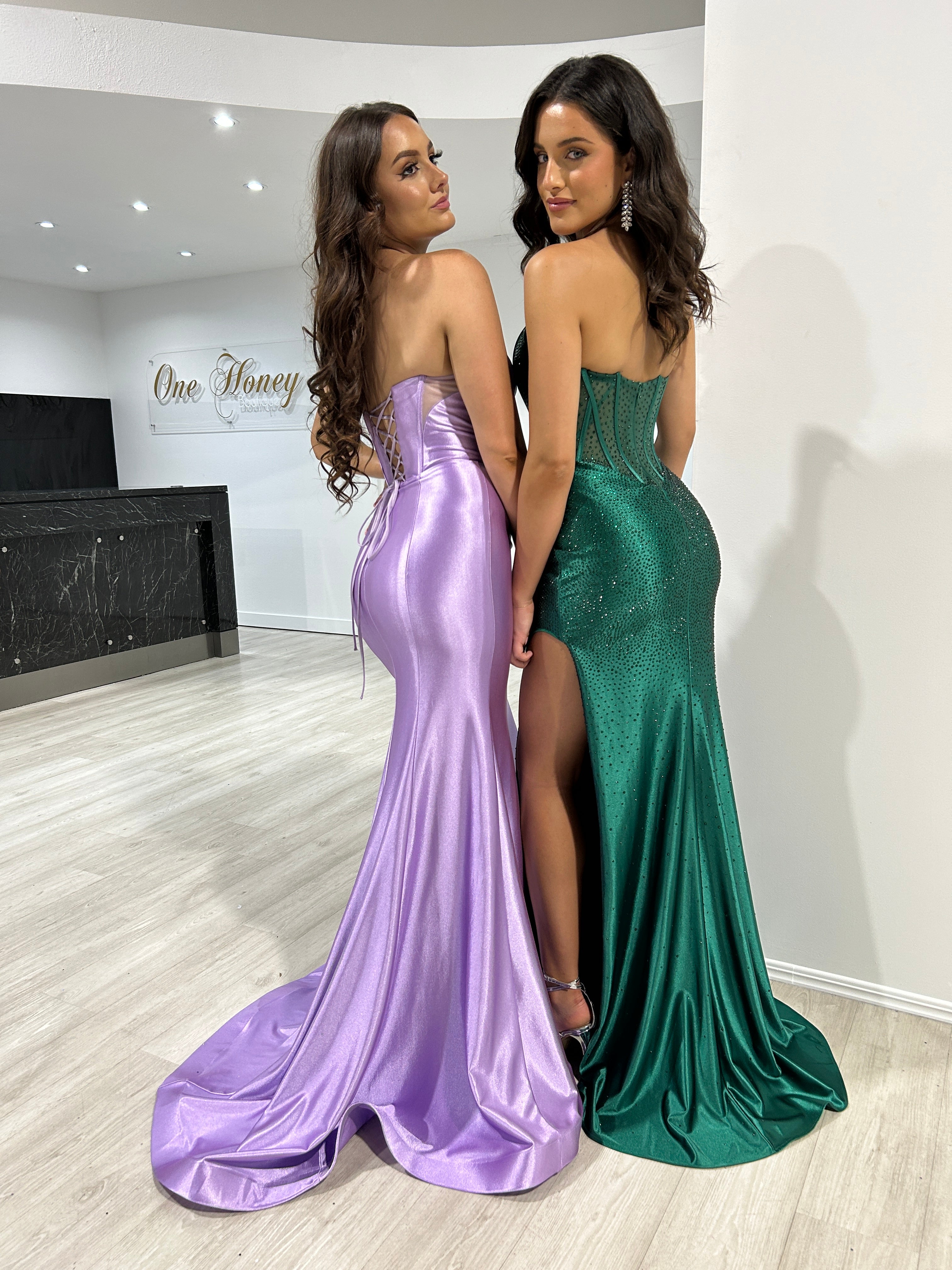 Two models in strapless satin evening gowns, one in lilac and one in emerald, with corset details. Ideal formal wear from Brisbane to Gold Coast.