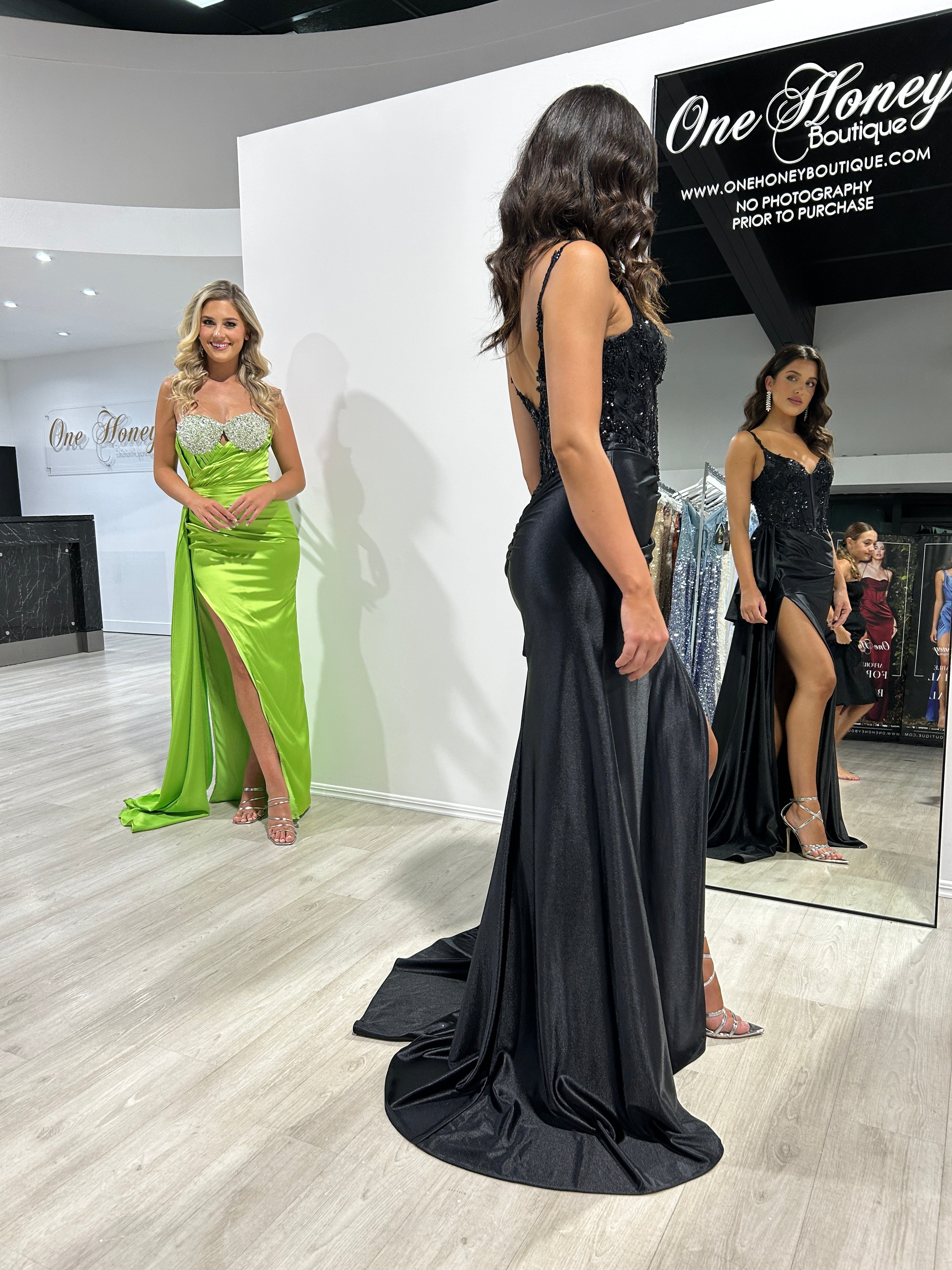 Women in elegant satin evening gowns at fashion boutique, one in black lace corset and one in green with slit. Brisbane to Gold Coast