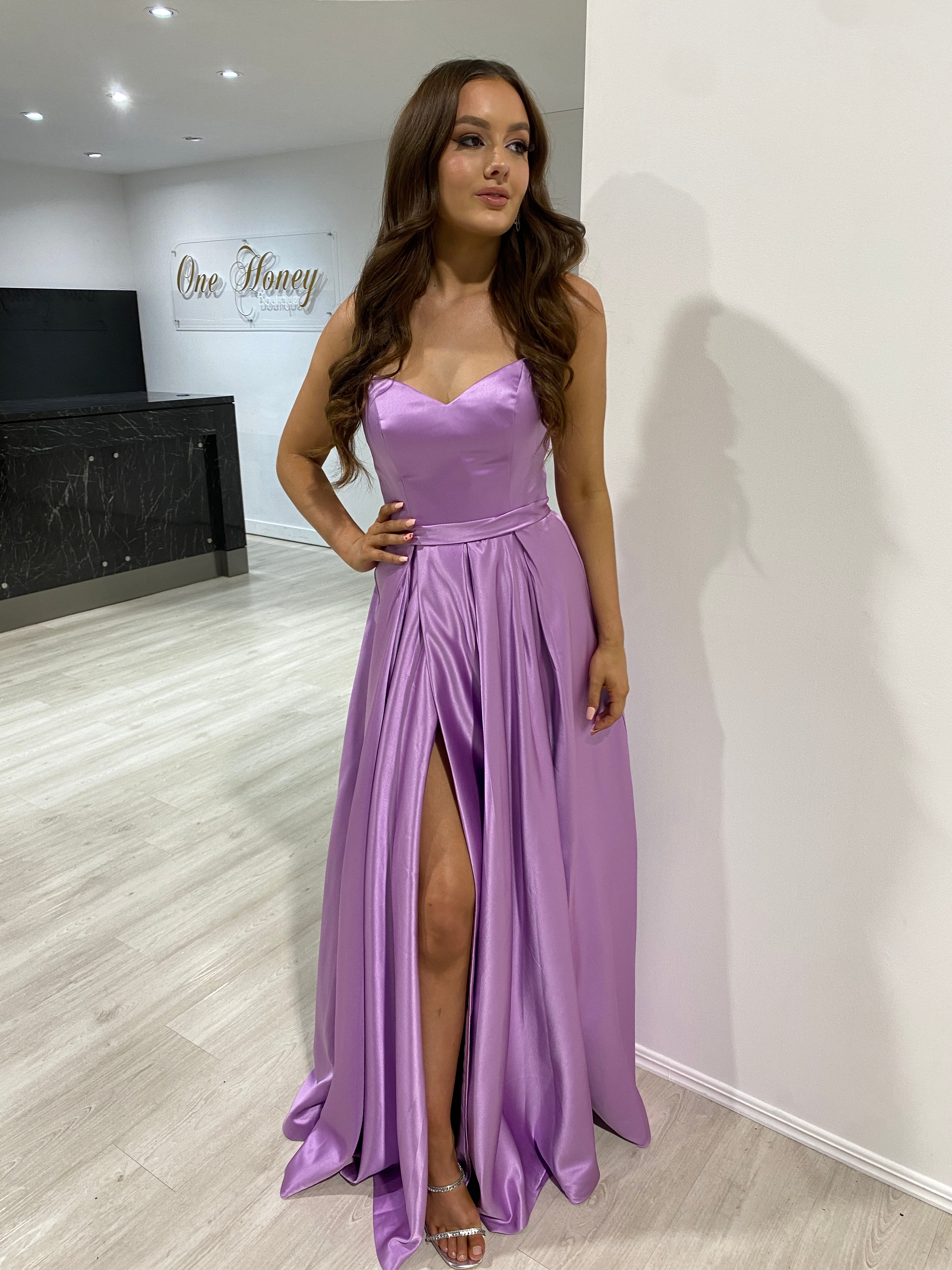 Woman in a purple Honey Couture DANIELLA formal dress with V front corset, lace-up back, and box pleat skirt, perfect for pageants.