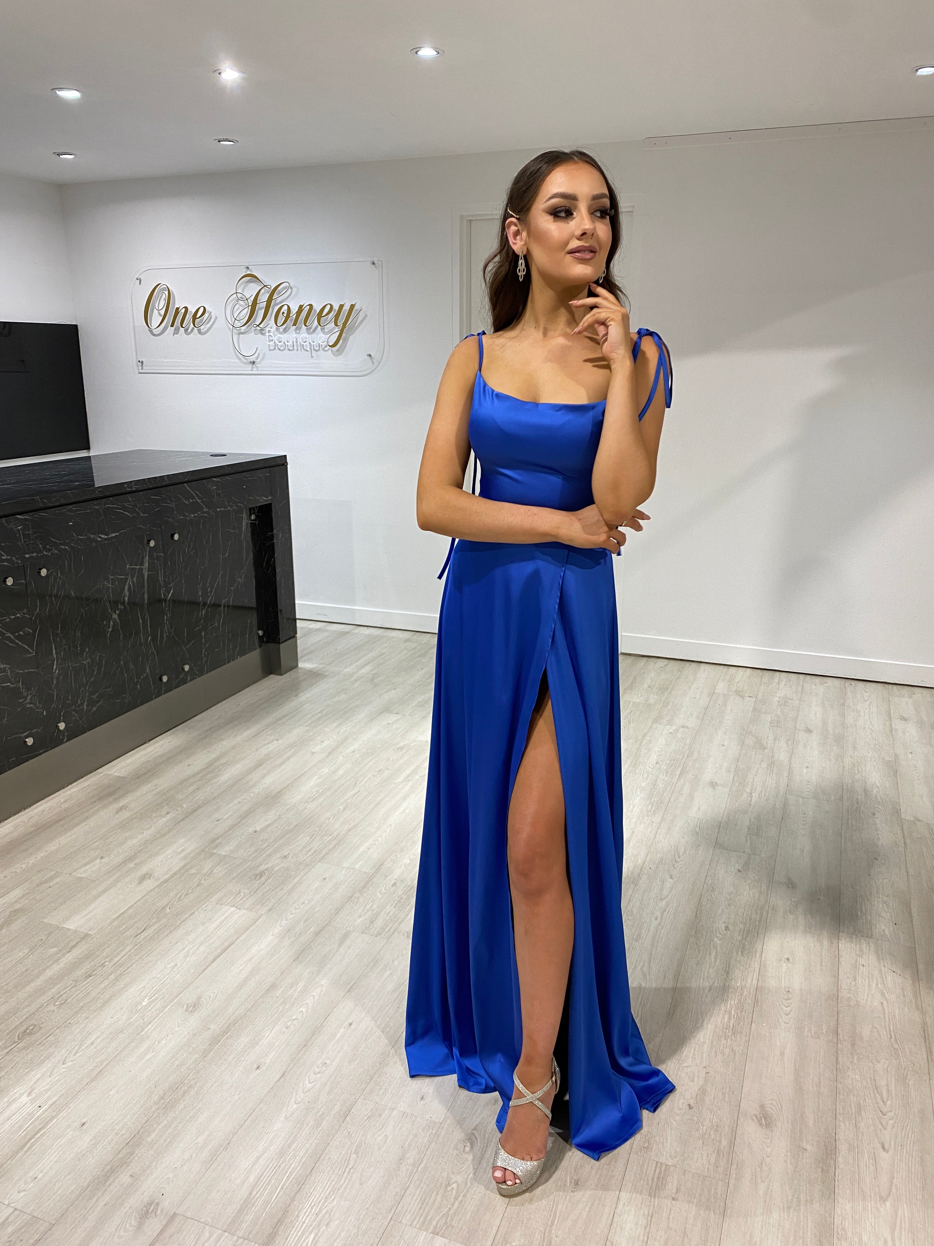 Woman in Honey Couture XENIA blue formal dress with tie-up straps, leg split, and slight train from Australian Designer. Ideal for prom or evening.