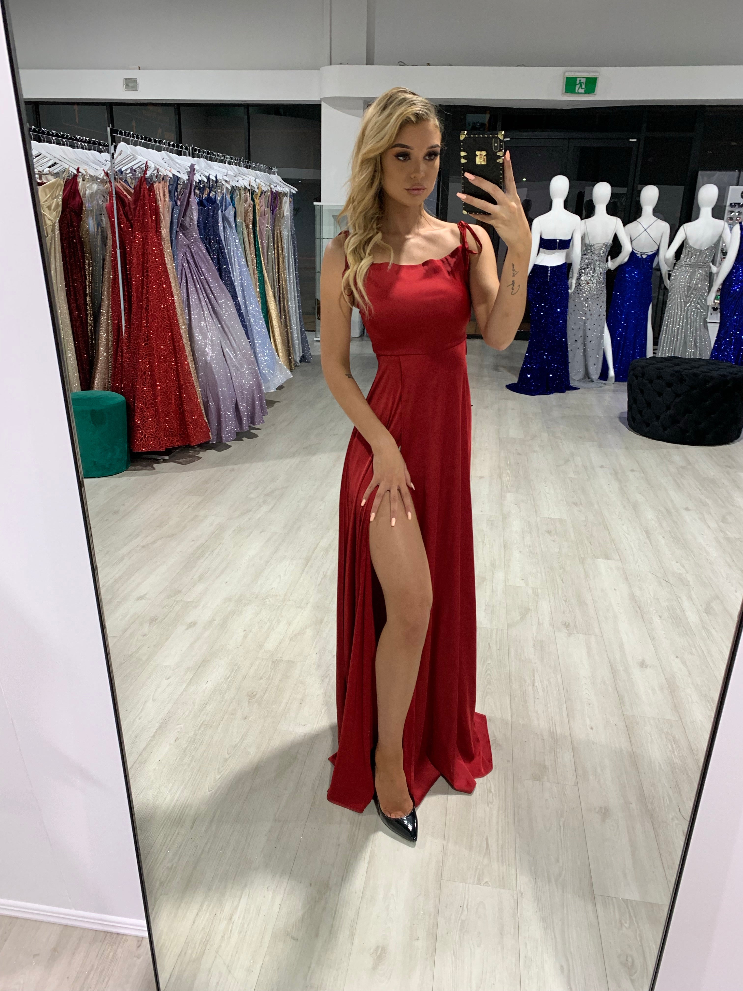 Woman wearing Honey Couture XENIA Burgundy Tie Up Formal Dress with leg split, by Australian Designer, in a boutique setting.