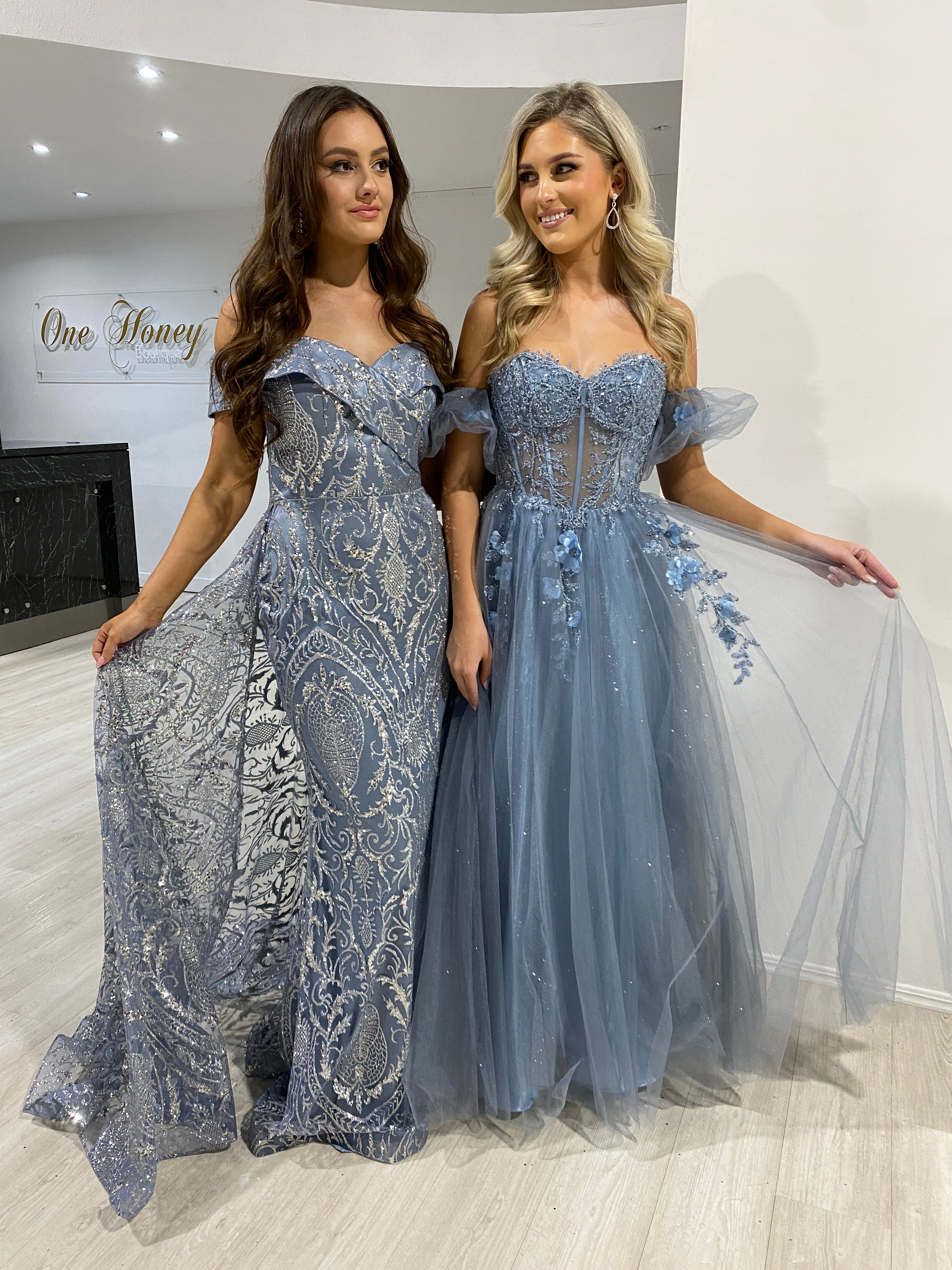 Two models wearing blue Honey Couture off-shoulder shimmer gowns, showcasing Australian designer prom and evening fashion.