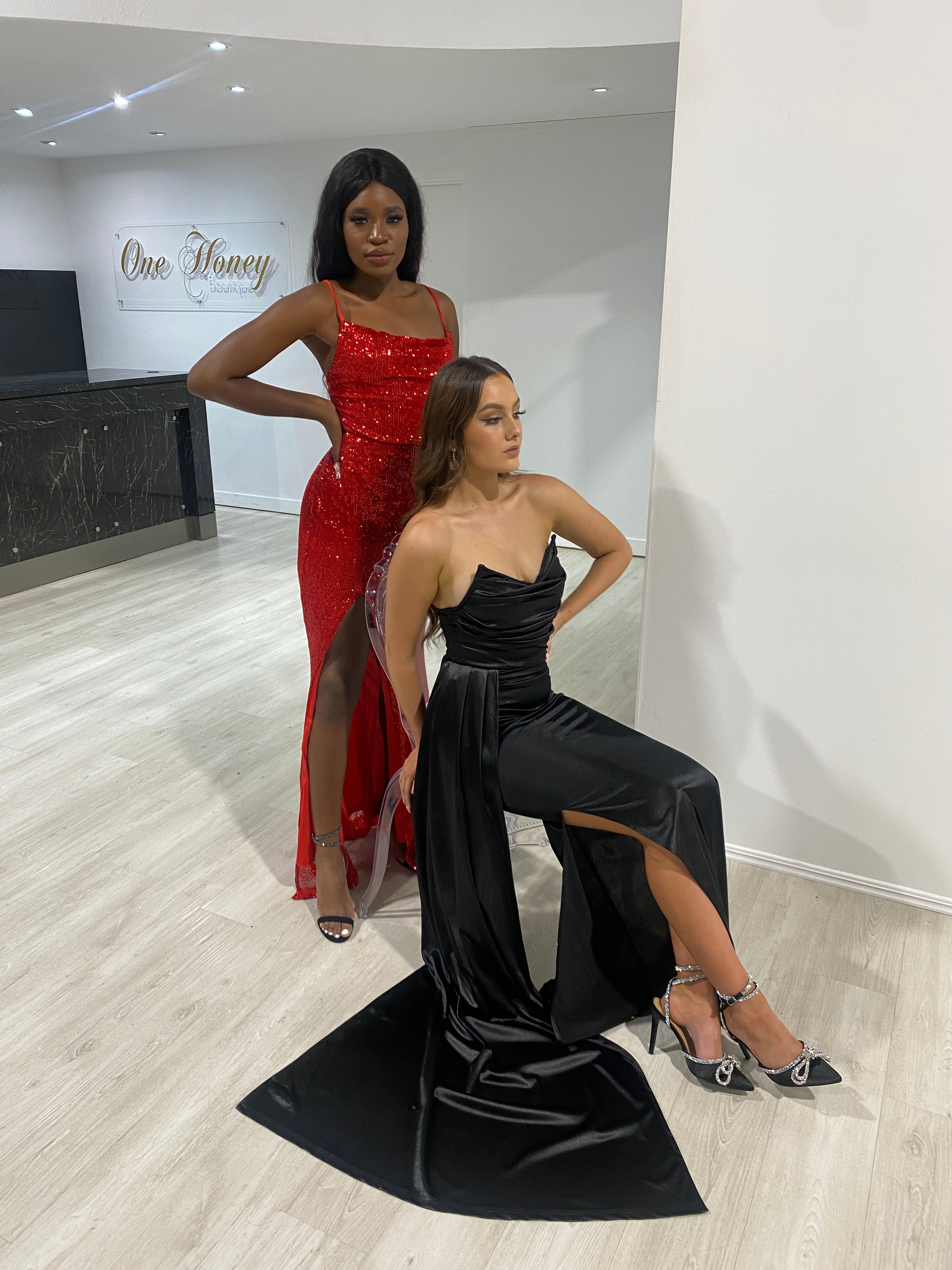 Models wearing Honey Couture ANGELIQUE Red Sequin Lace Up Dress and black evening gown by Australian Designer in a showroom.