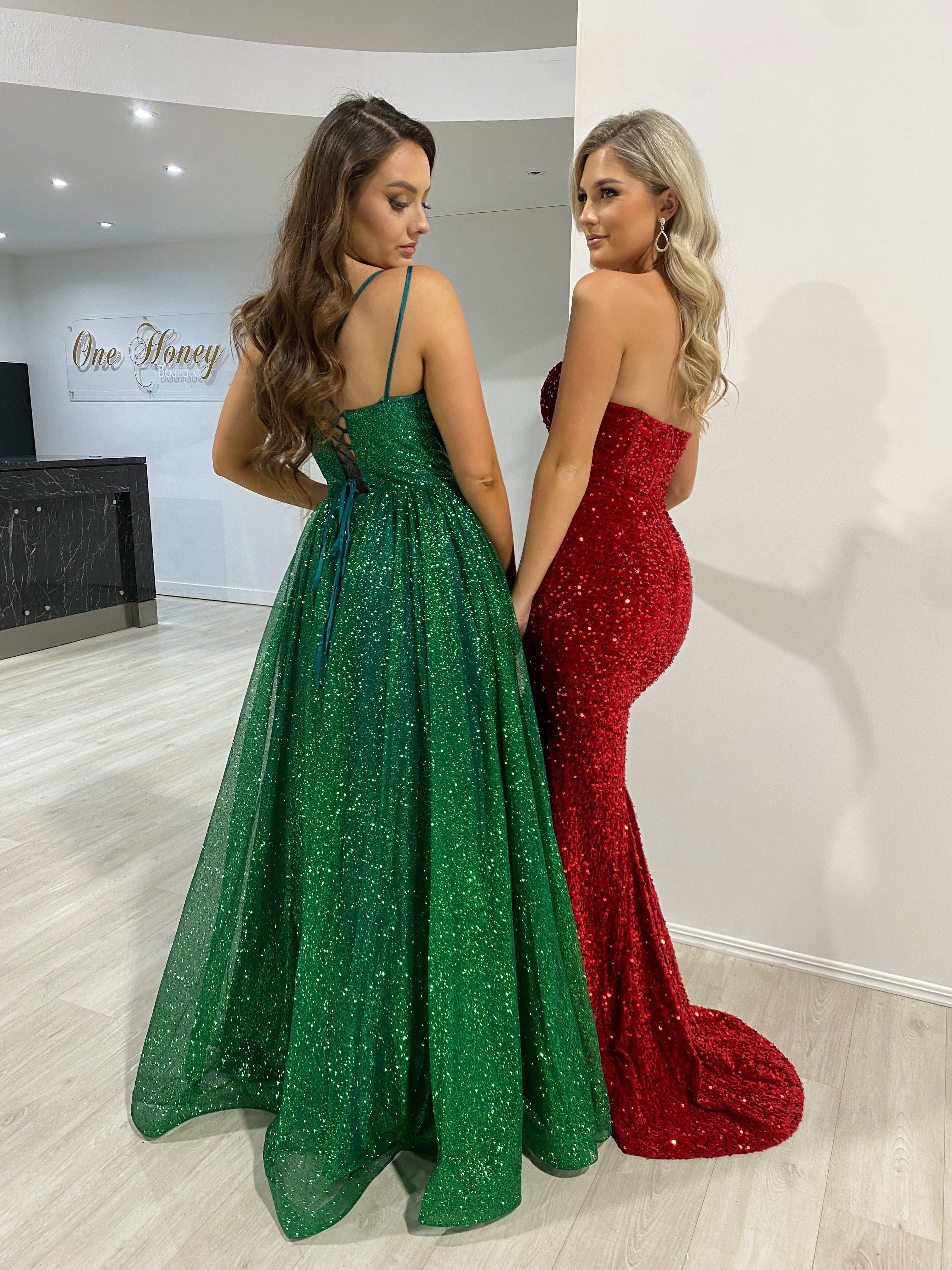 Two women in Honey Couture evening gowns, one in a red strapless MADDISON mermaid dress and the other in a glittery green gown. Australian Designer.