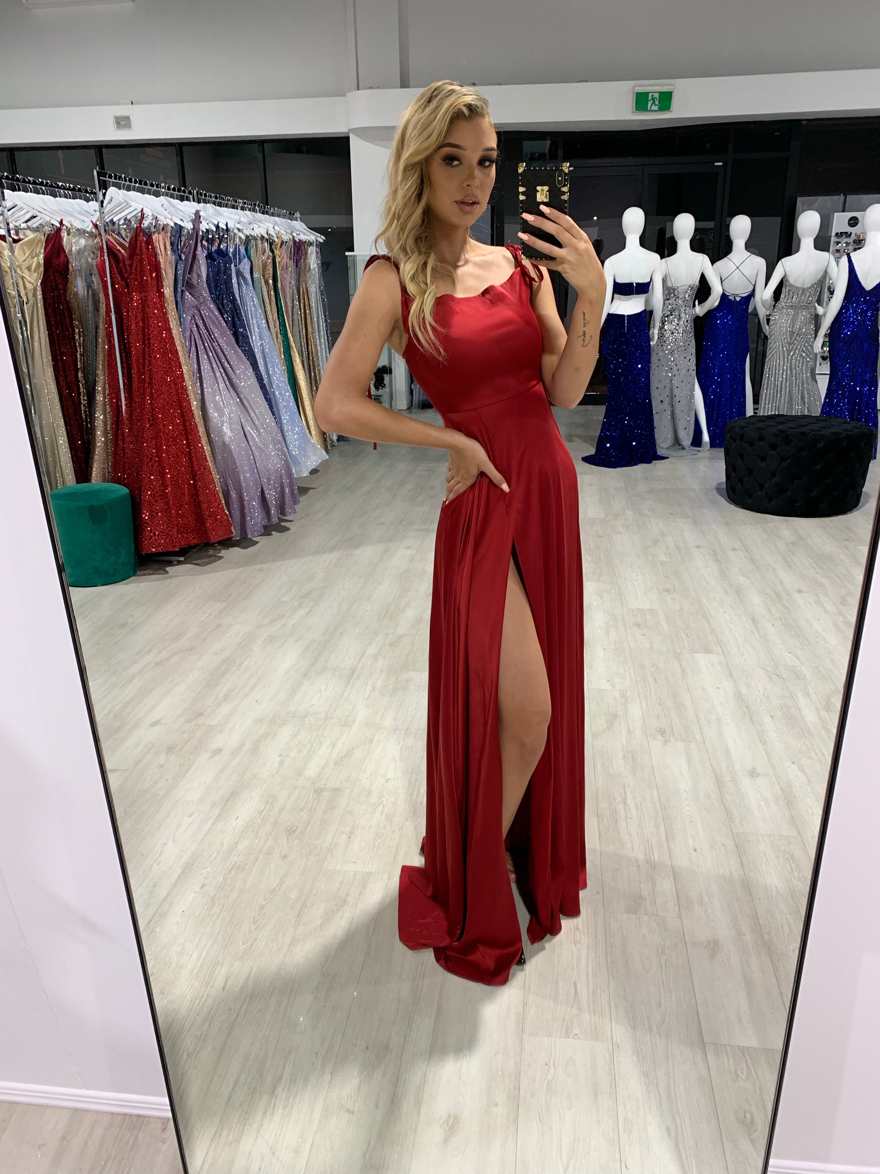 Woman wearing Honey Couture XENIA burgundy tie up formal bridesmaid dress with leg split, from Australian Designer, in store display.